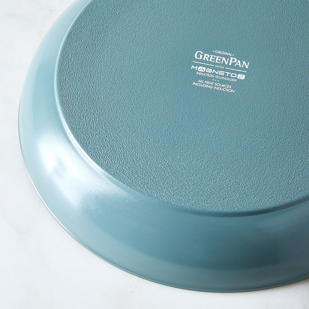 Nahaufnahme des Bodens einer teal GreenPan-Pfanne. Sie hat eine strukturierte Oberfläche und Markenlogos, inkl. Magneto-Induktion.