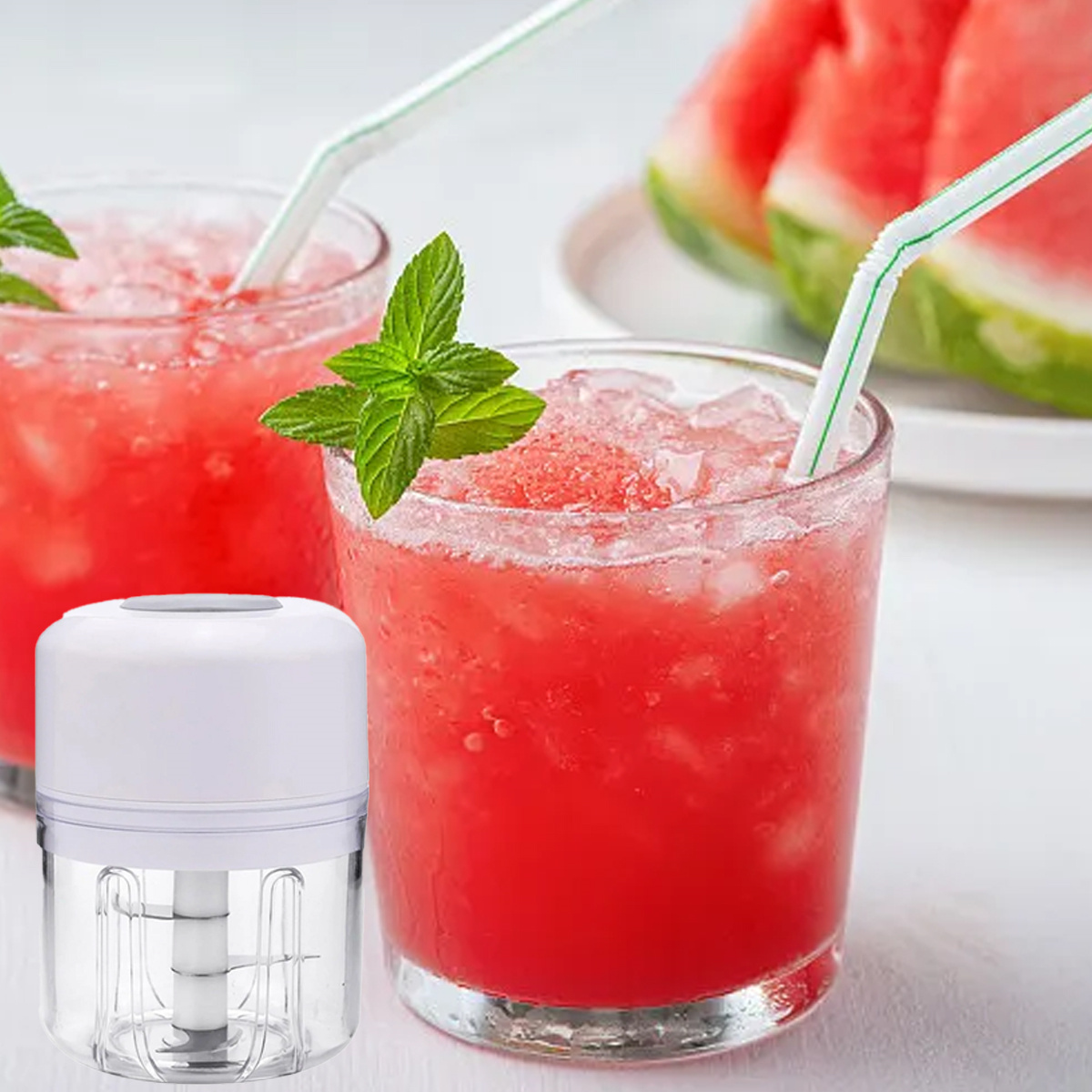 Zwei Gläser roter Wassermelonen-Saft mit Eis und Strohhalmen, Minzblättern und einem kleinen weißen Küchenmixer, mit Wassermelonenscheiben.