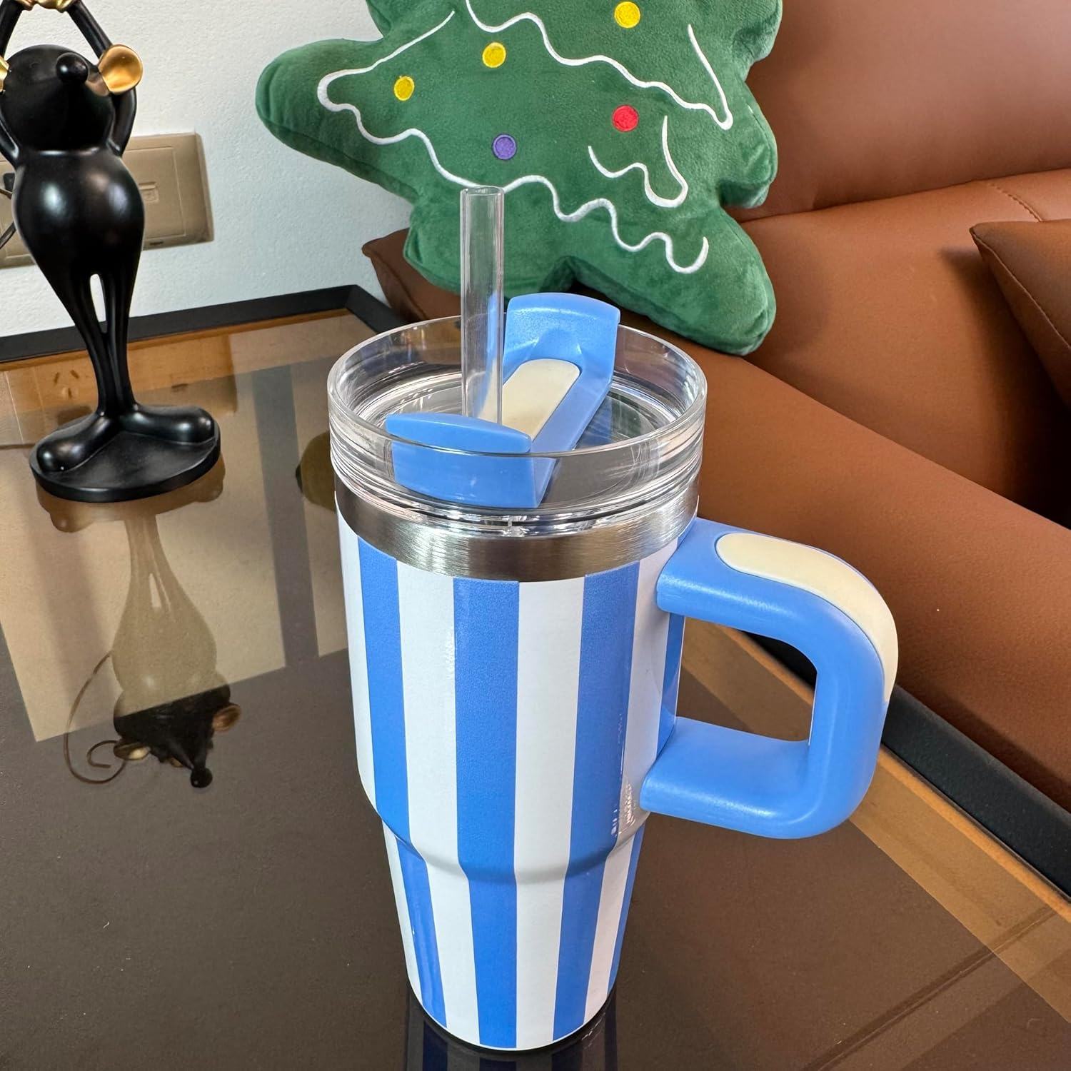 Ein Becher mit blau-weißen Streifen. Er hat einen blauen Griff und Deckel. Im Hintergrund ist ein grünes Weihnachtsbaumkissen.