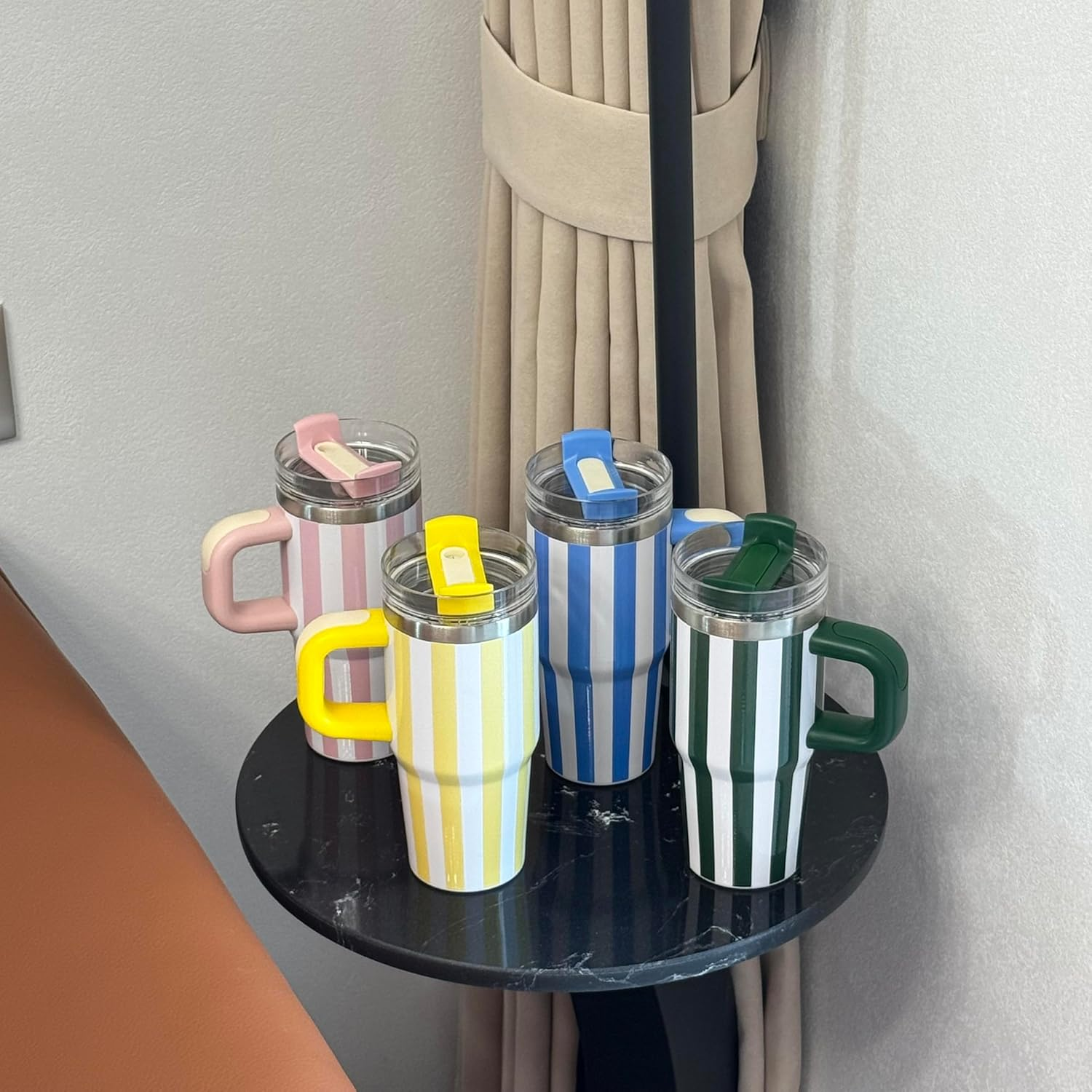 Vier bunte, gestreifte Becher mit Griffen stehen auf einem schwarzen Tisch. Die Becher sind rosa, gelb, blau und grün.