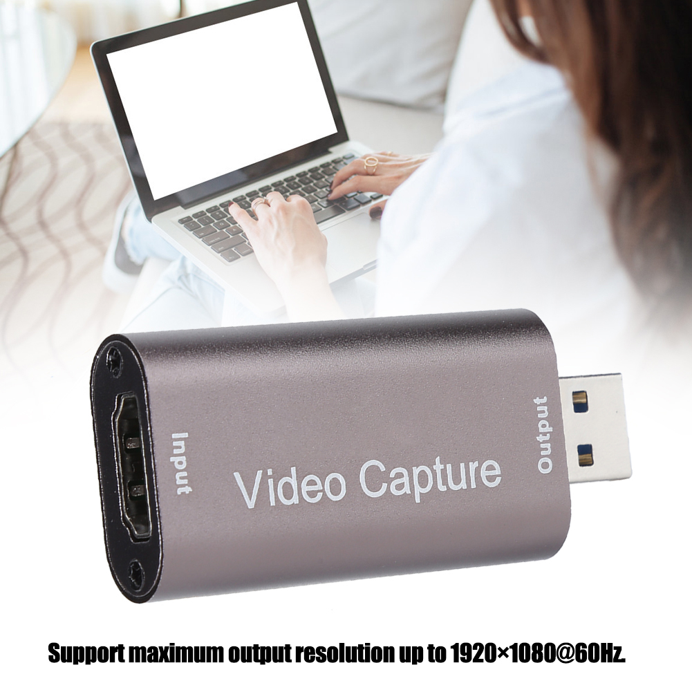 Ein Videoaufnahmegerät mit HDMI- und USB-Anschlüssen. Im Hintergrund benutzt eine Person einen Laptop.