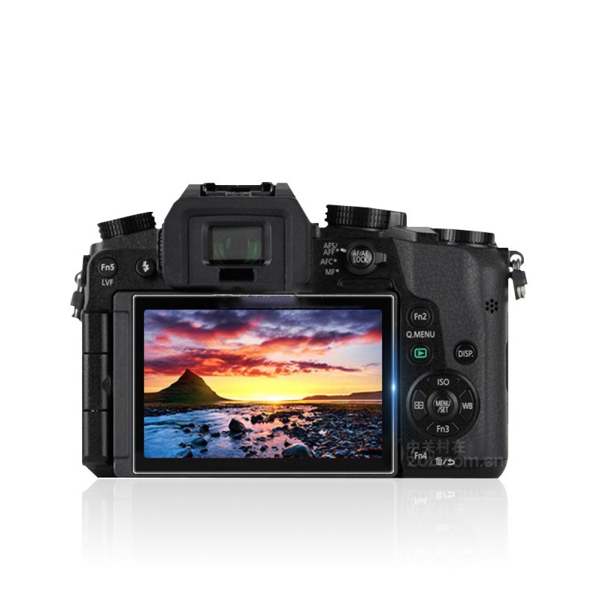 Una fotocamera nera mostra un tramonto su una montagna e acqua. Pulsanti e quadranti visibili. La fotocamera si riflette su una superficie bianca.