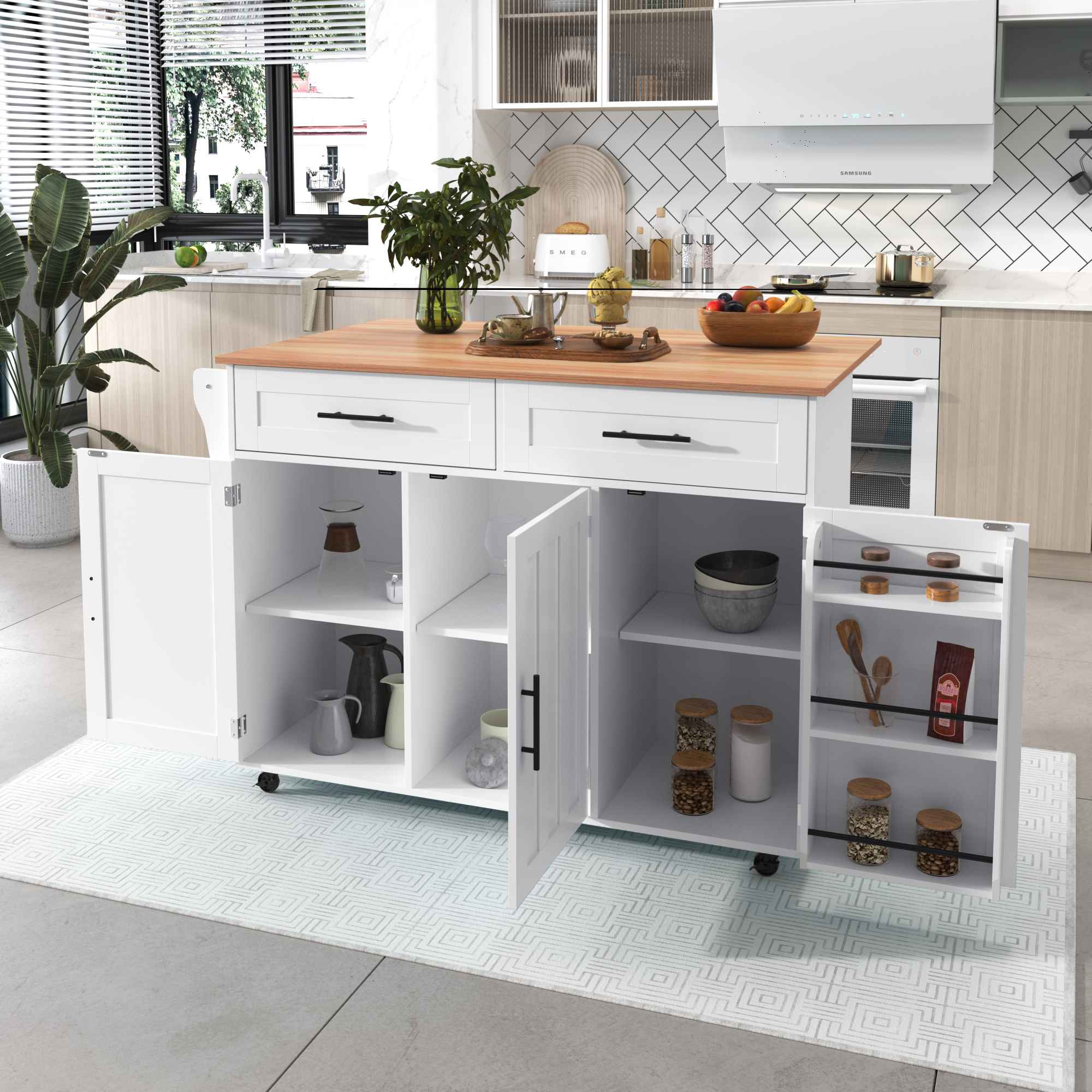 Kücheninsel mit Holzplatte, weißen Schränken, Schubladen und offenen Regalen. Enthält Gläser, Utensilien und Pflanzen. Küche im Hintergrund.