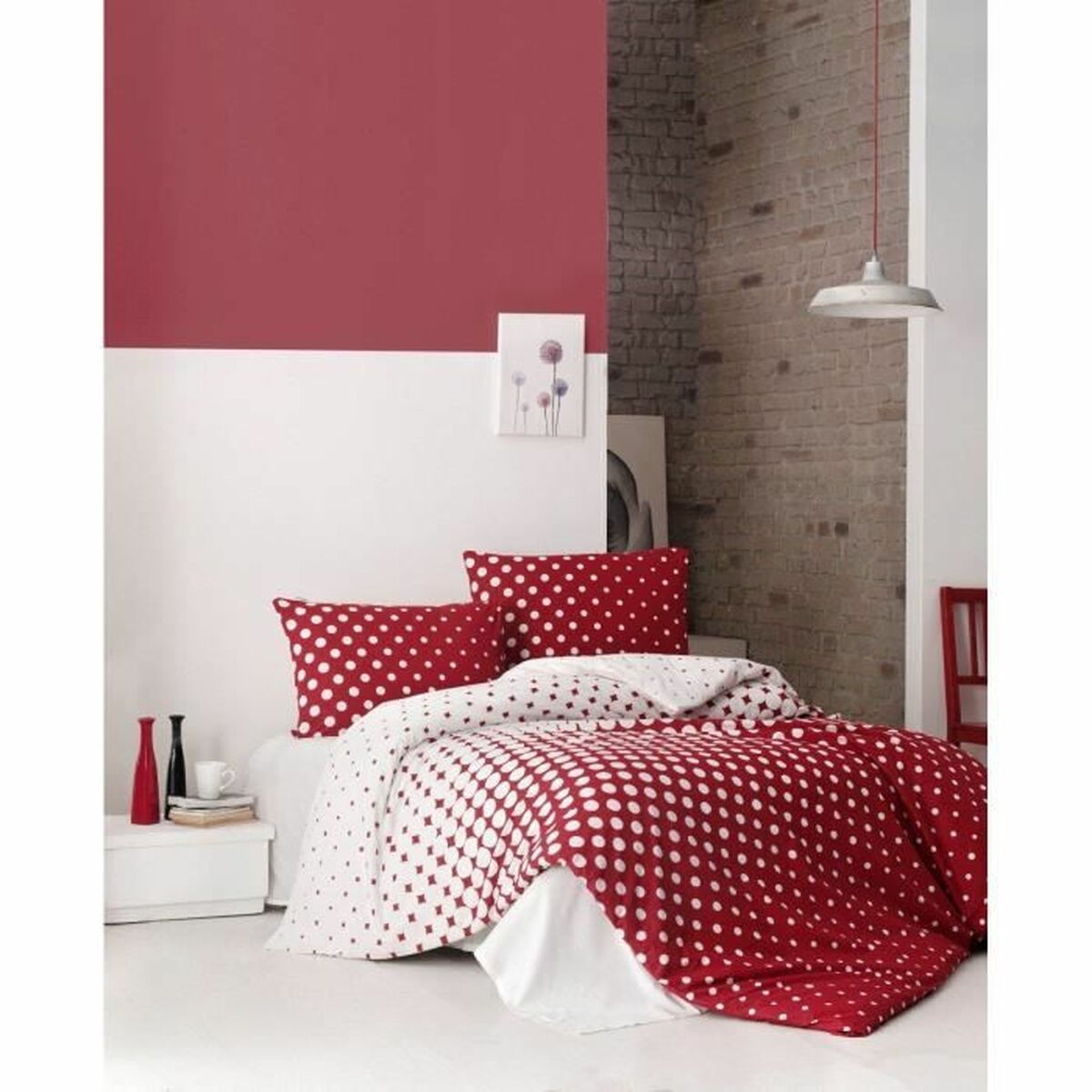 Rote und weiße Polka-Dot-Bettwäsche auf einem Bett. Rote Wand dahinter. Weißer Nachttisch mit Vasen. Backsteinmauer im Hintergrund.