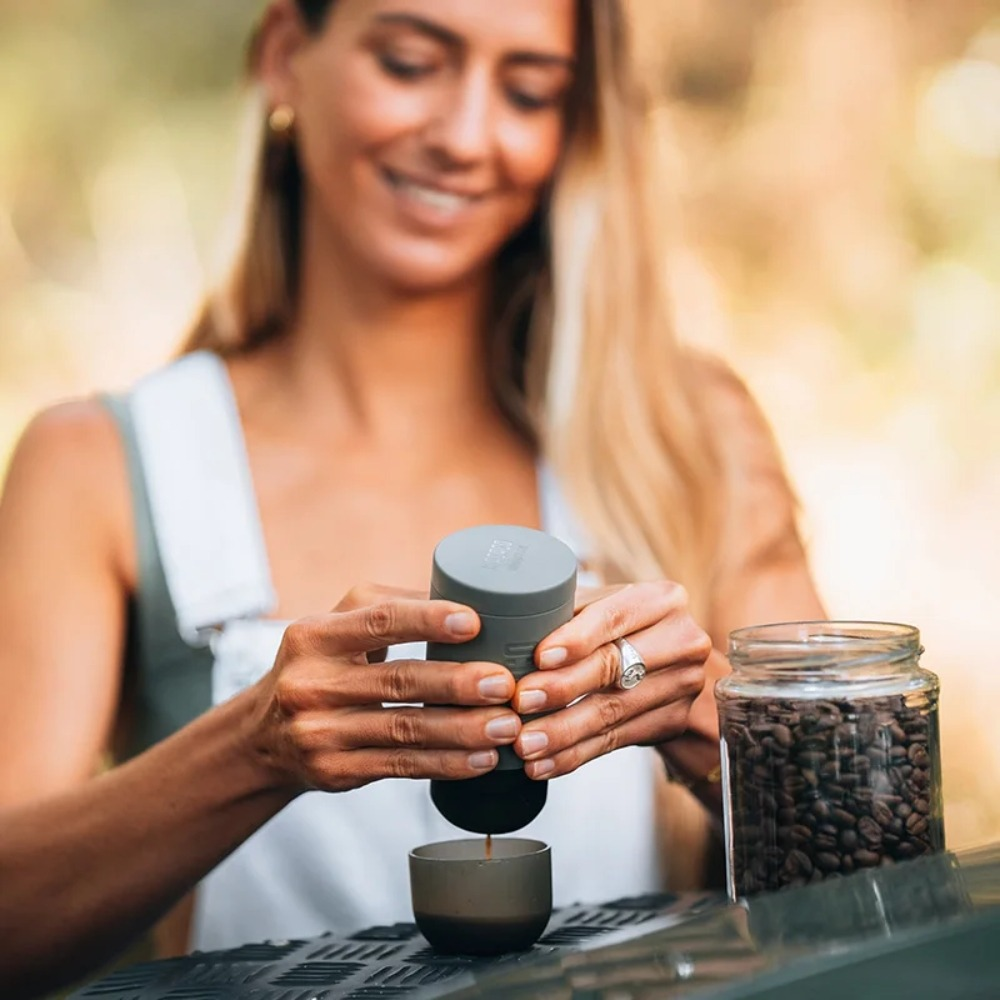 Frau bereitet Kaffee mit einem tragbaren Espressokocher zu. Kaffeebohnen in einem Glas sind in der Nähe.