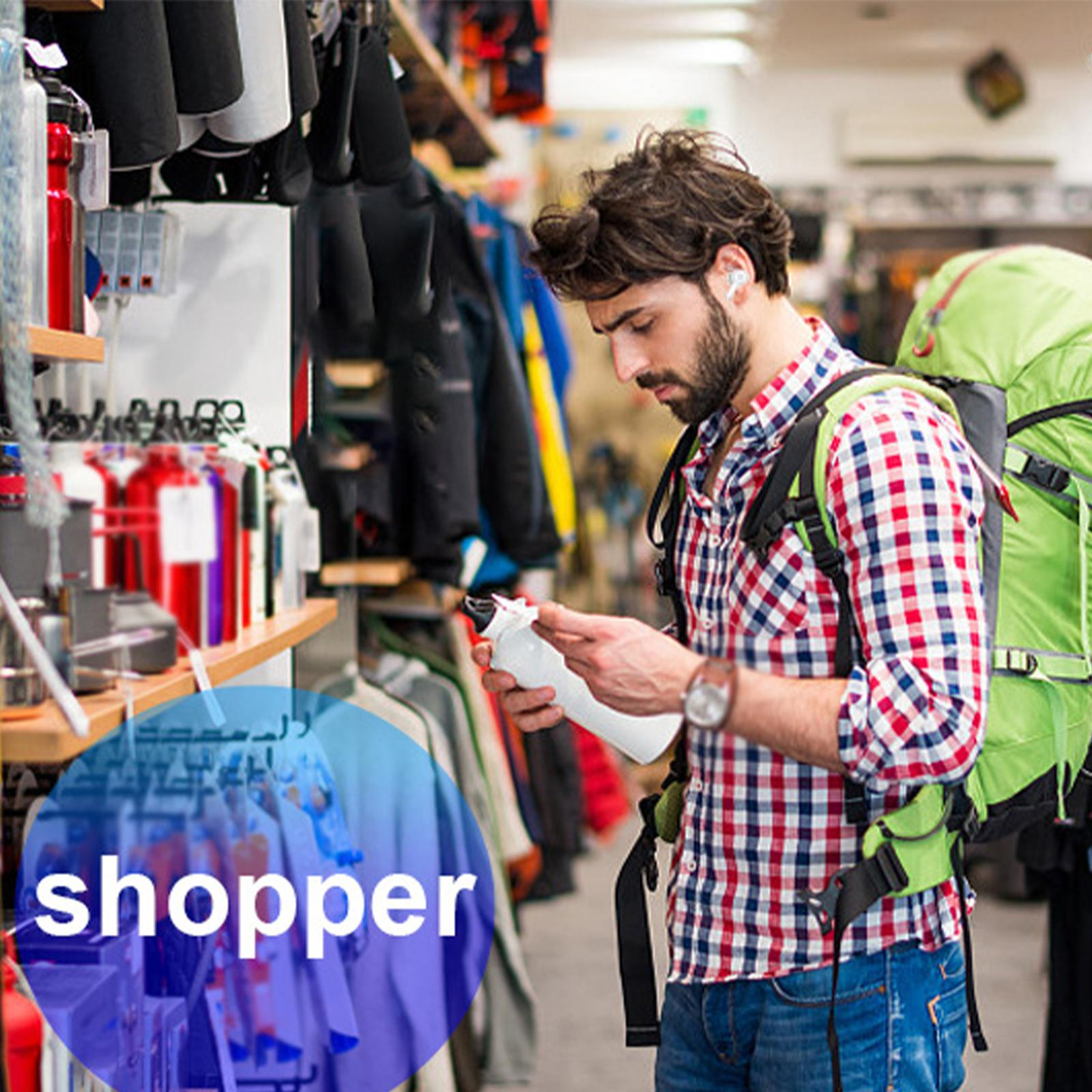 Ein Mann mit Rucksack betrachtet eine Flasche in einem Geschäft. Regale mit Produkten und Kleidung befinden sich im Hintergrund.