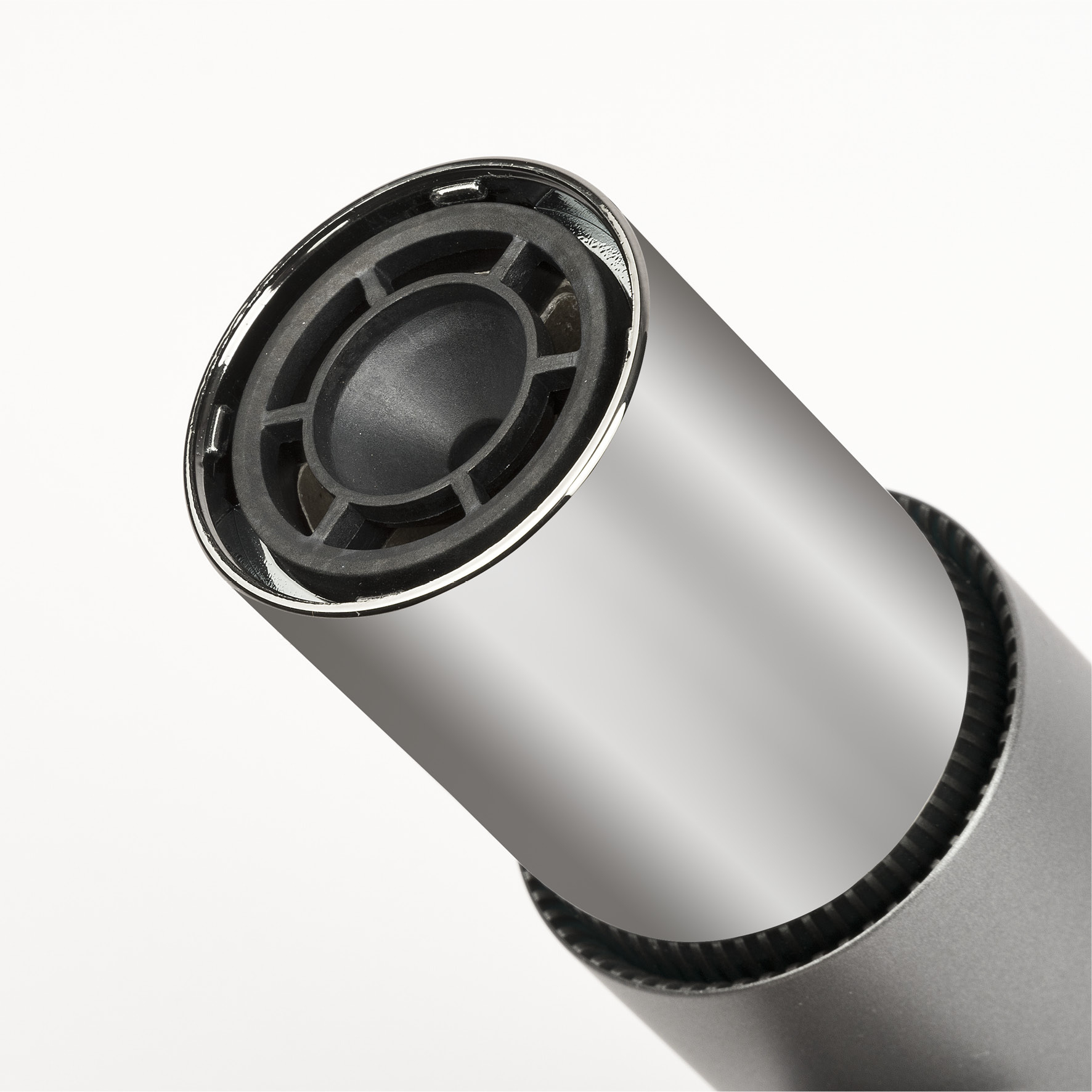 Zbliżenie metalowej dyszy suszarki do włosów. Dysza jest srebrna, z czarnym, wzorzystym wnętrzem. Tło jest białe.