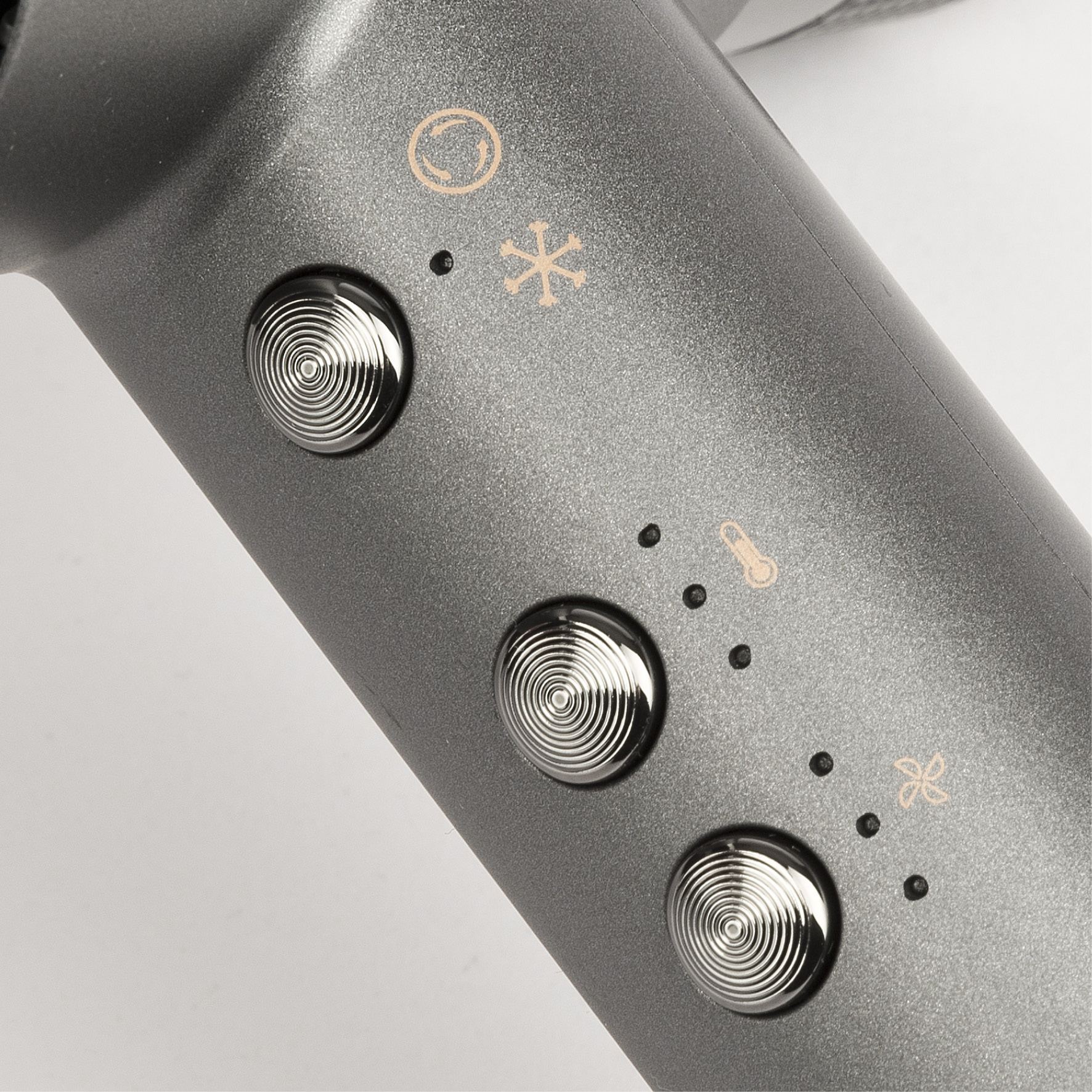 Zbliżenie szarej suszarki do włosów z trzema srebrnymi przyciskami i ikonami sterowania. Tło jest białe.