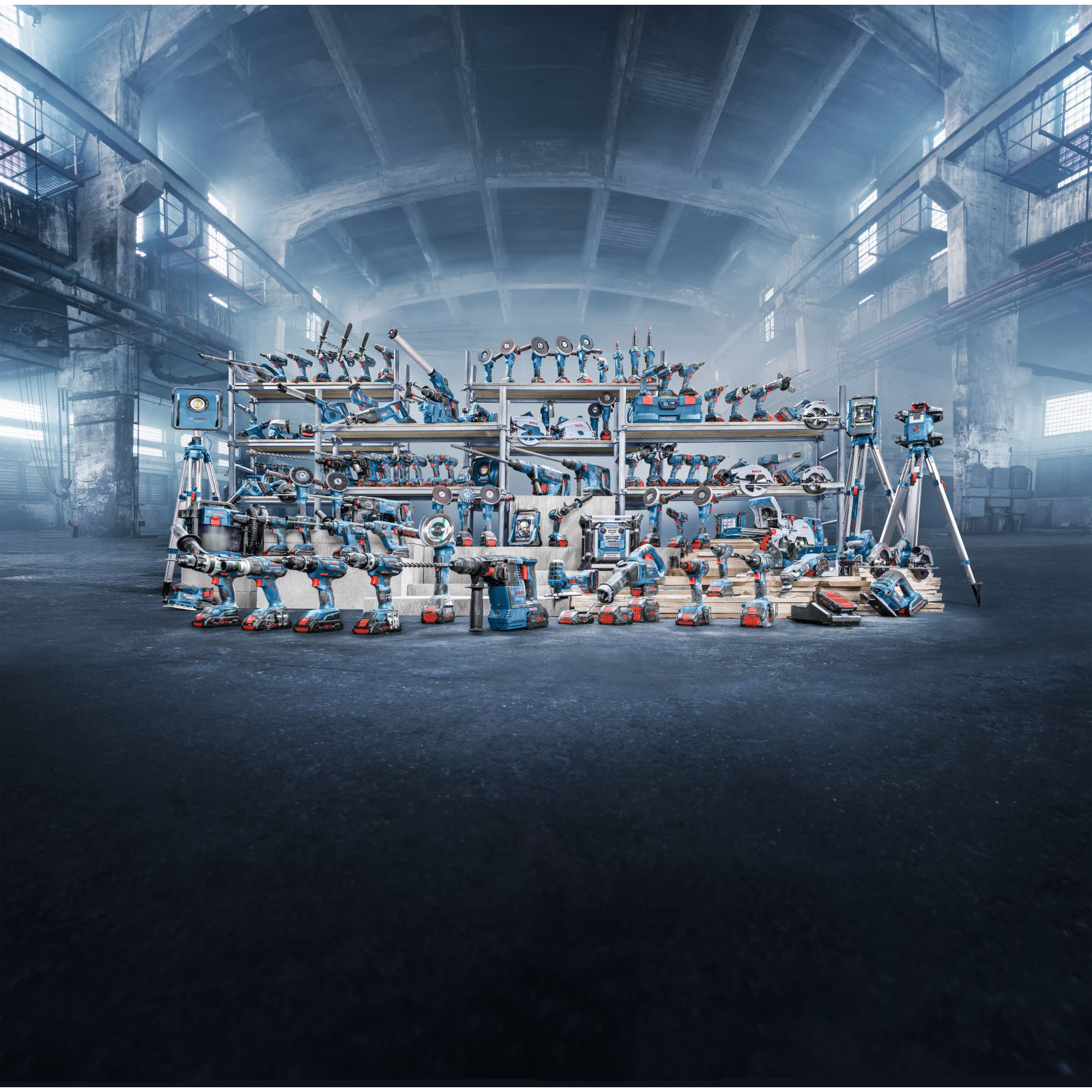 Vielfalt an blauen und roten Elektrowerkzeugen auf Regalen und Boden in einem großen Industriegebäude.