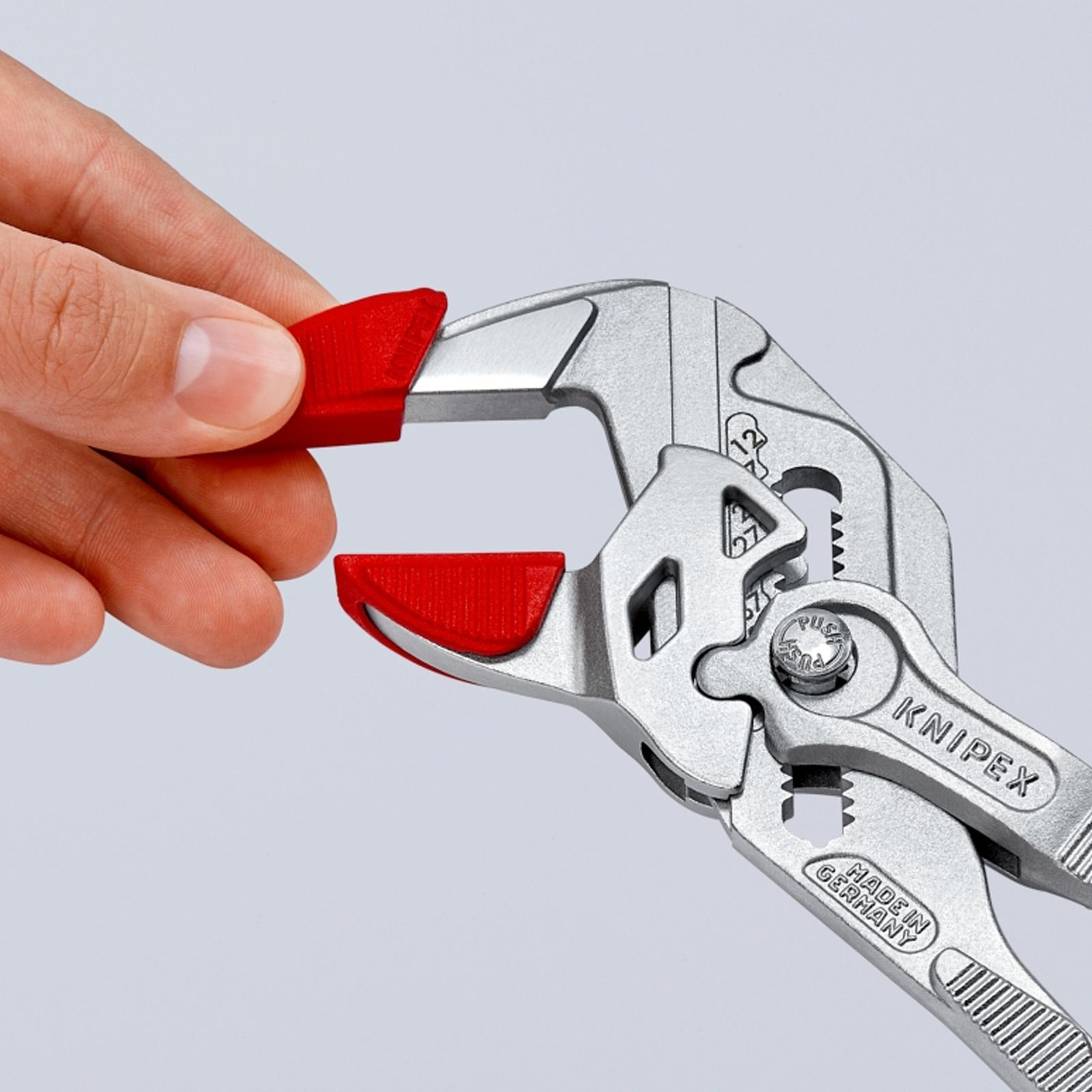Hand holding a silver wrench with red rubber tips. The wrench is marked 'KNIPEX' and 'MADE IN GERMANY'.