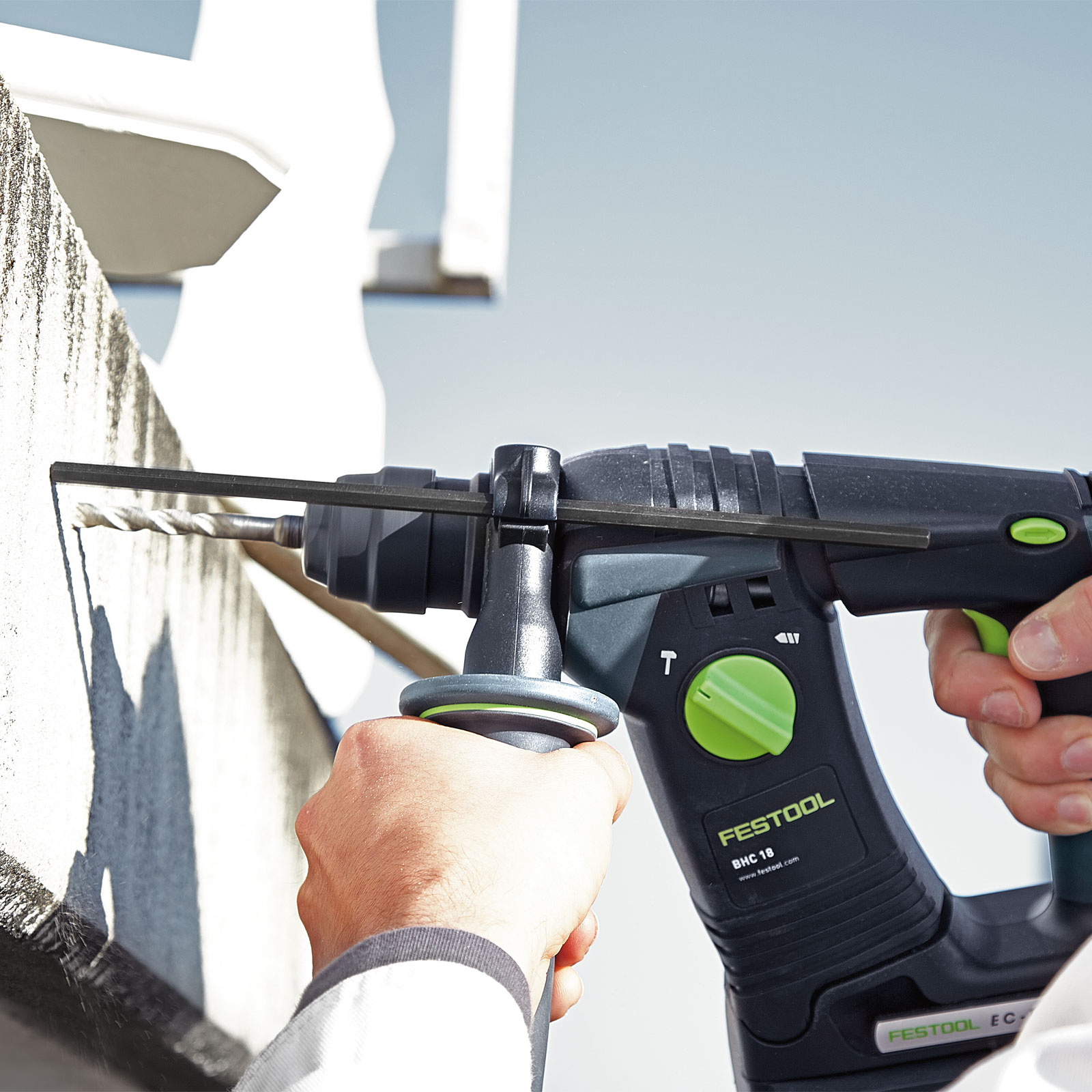 Una persona sta usando un trapano nero e verde per forare un muro bianco. Il trapano è etichettato Festool BHC 18.