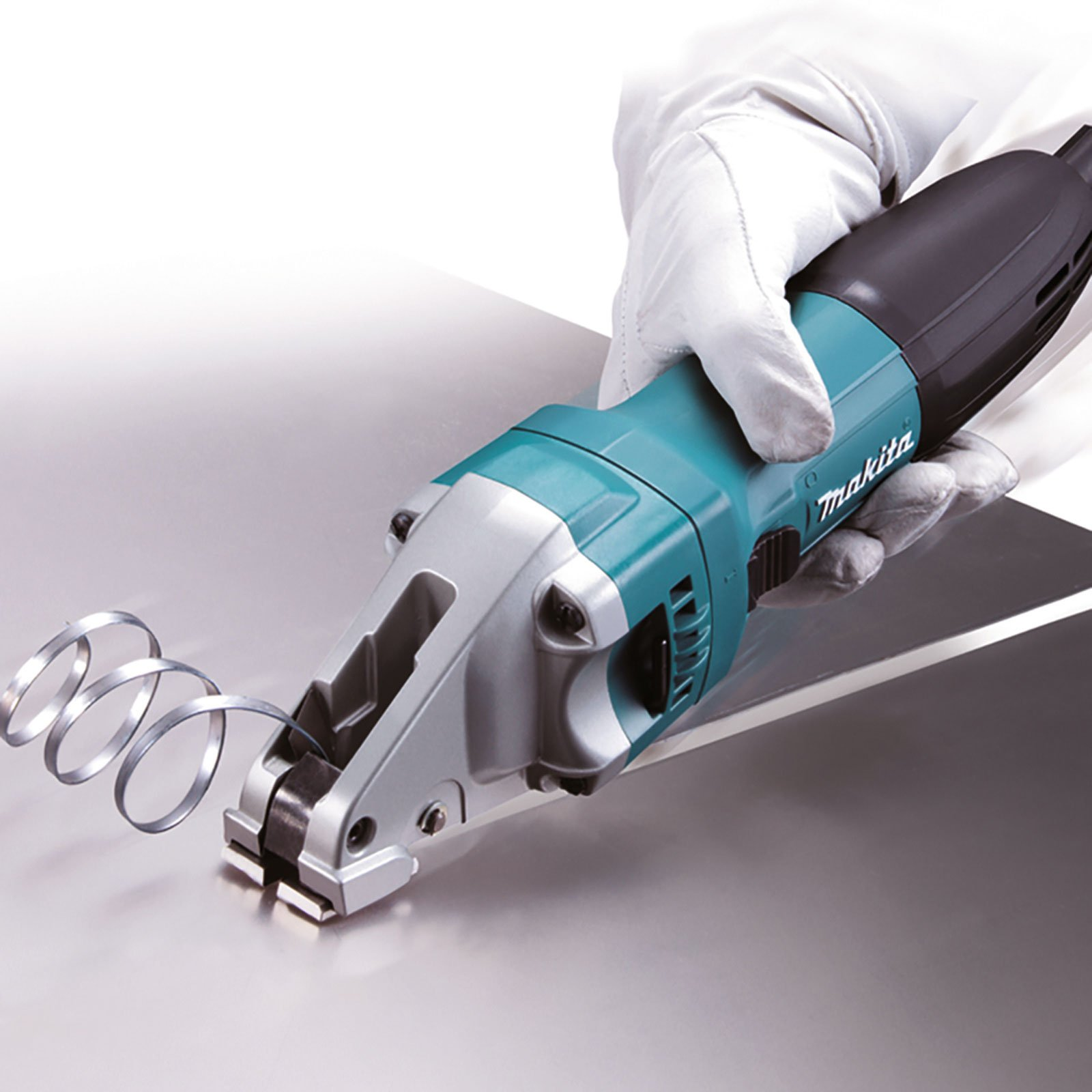 Eine Hand in einem weißen Handschuh hält eine teal- und schwarze Makita-Blechschere und schneidet ein Blech. Metallspäne kräuseln sich weg.