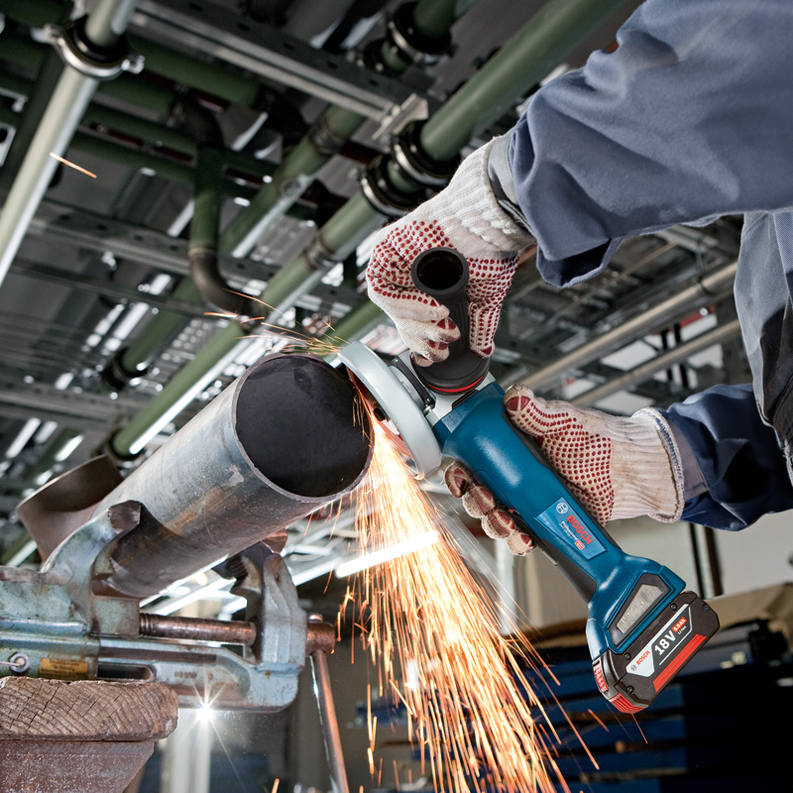 Robot szlifuje rurę narzędziem elektrycznym, lecą iskry. Rura jest trzymana w imadle.