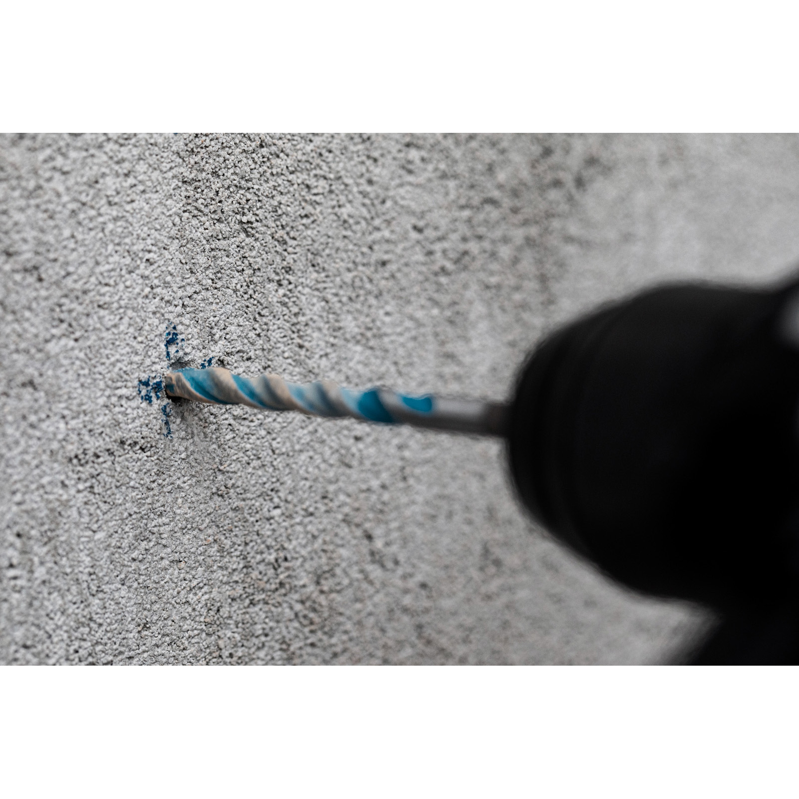 Ein Bohrer bohrt in eine graue Betonmauer. Der Bohrer hat blaue und silberne Spiralen, und der Bohrer ist schwarz.