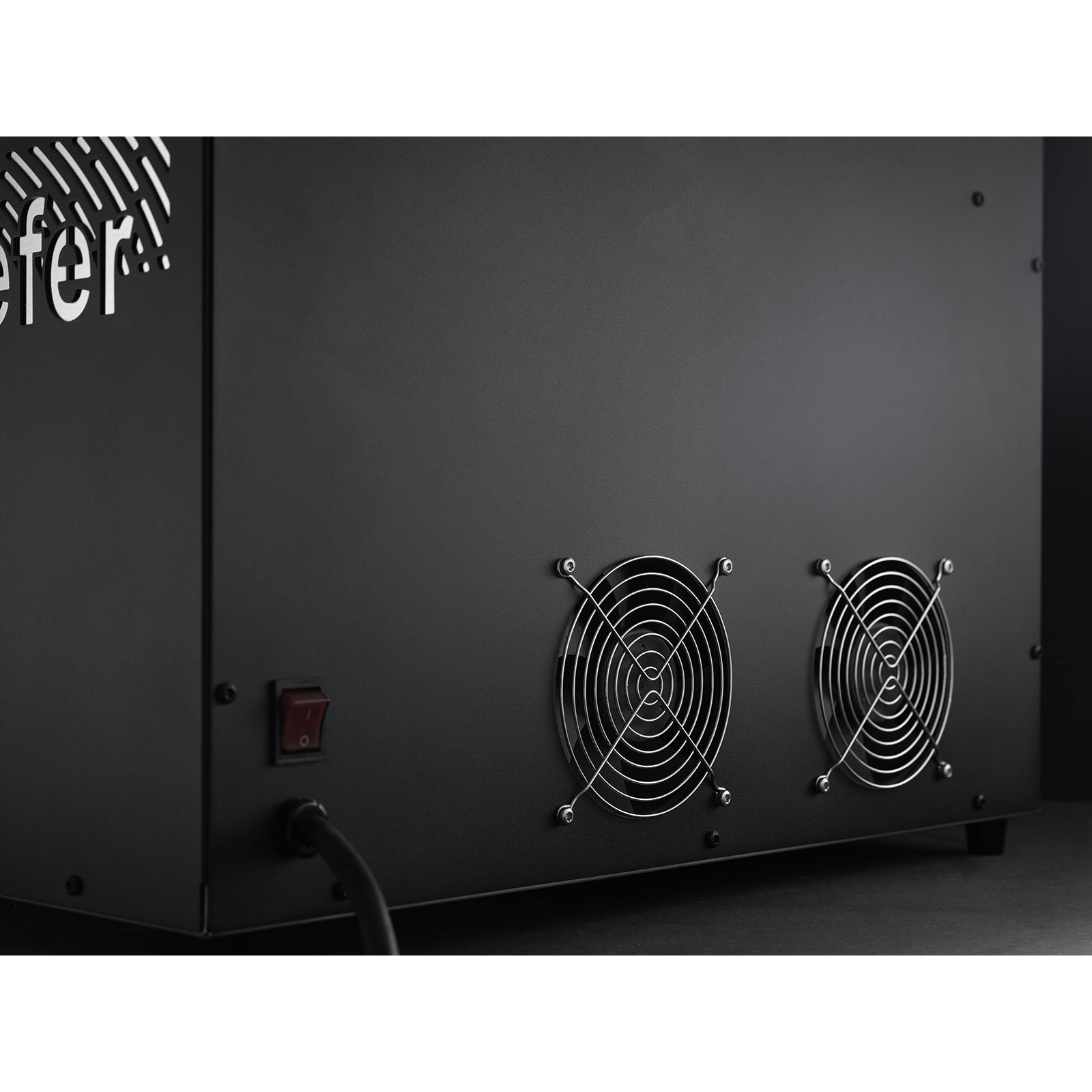 Schwarze Metallbox mit Lüftern, Schalter und Netzkabel. Die Box hat ein Logo. Der Hintergrund ist eine dunkle Oberfläche.