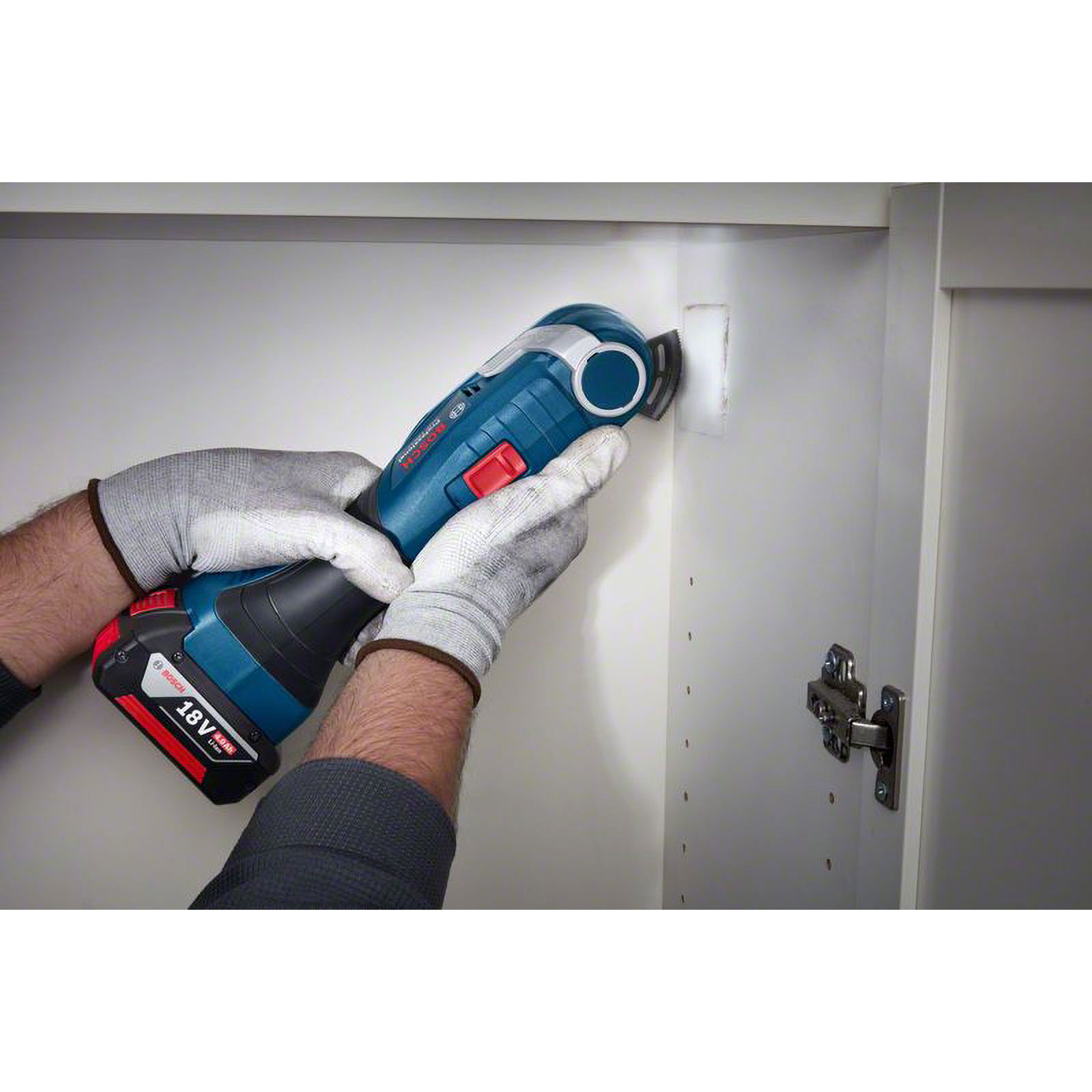 Una persona usa una multiherramienta Bosch para cortar un agujero en un gabinete blanco. La persona usa guantes.