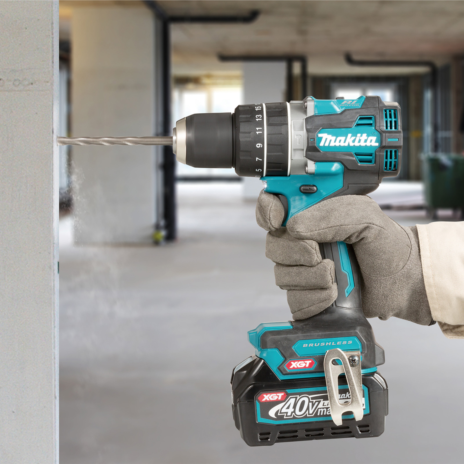 Una mano fora un muro con un trapano Makita. Il trapano è verde acqua e nero, con una batteria. Vengono indossati guanti grigi.