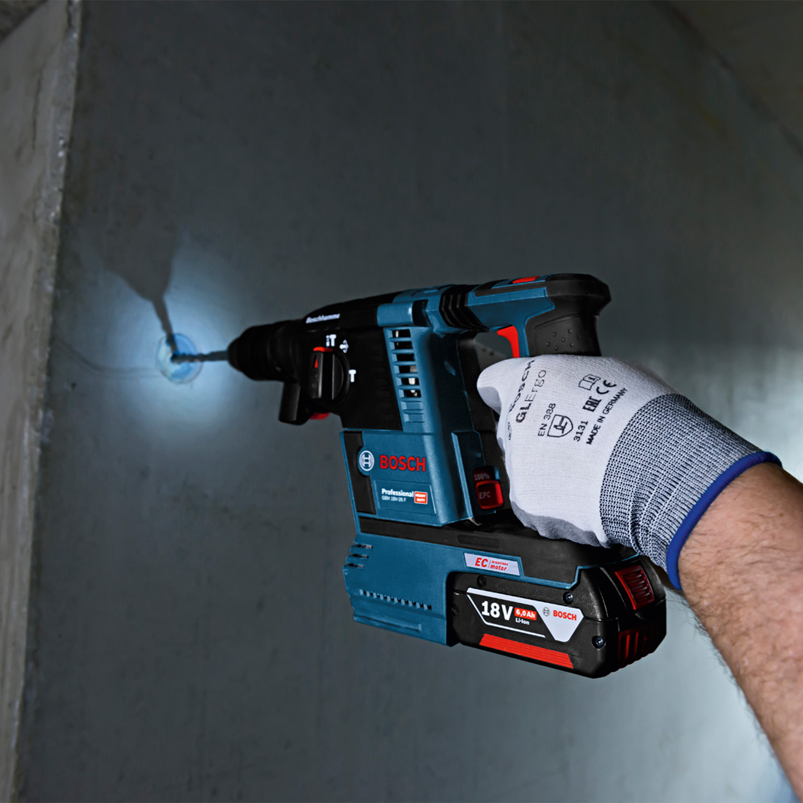 Eine Person bohrt mit einem Bosch-Bohrer in eine Wand. Der Bohrer ist blau und schwarz. Die Person trägt einen weißen Handschuh.