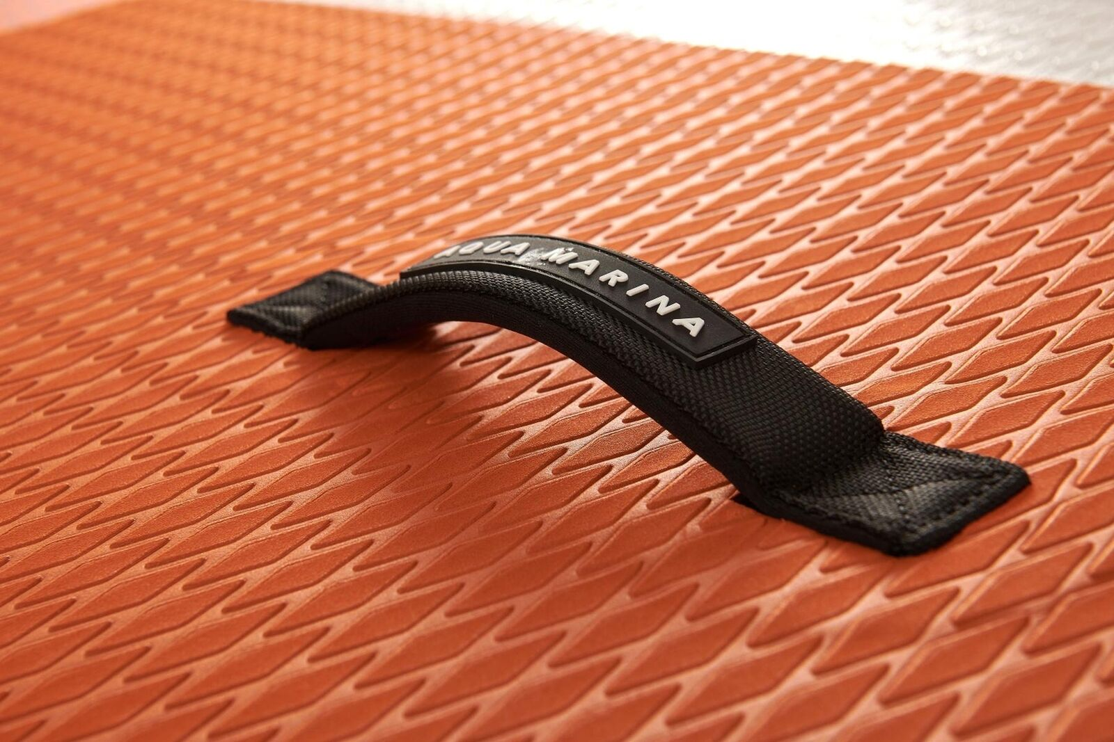 Nahaufnahme einer orangefarbenen Paddleboard-Oberfläche mit einem schwarzen Griff, der mit 'Aqua Marina' beschriftet ist.