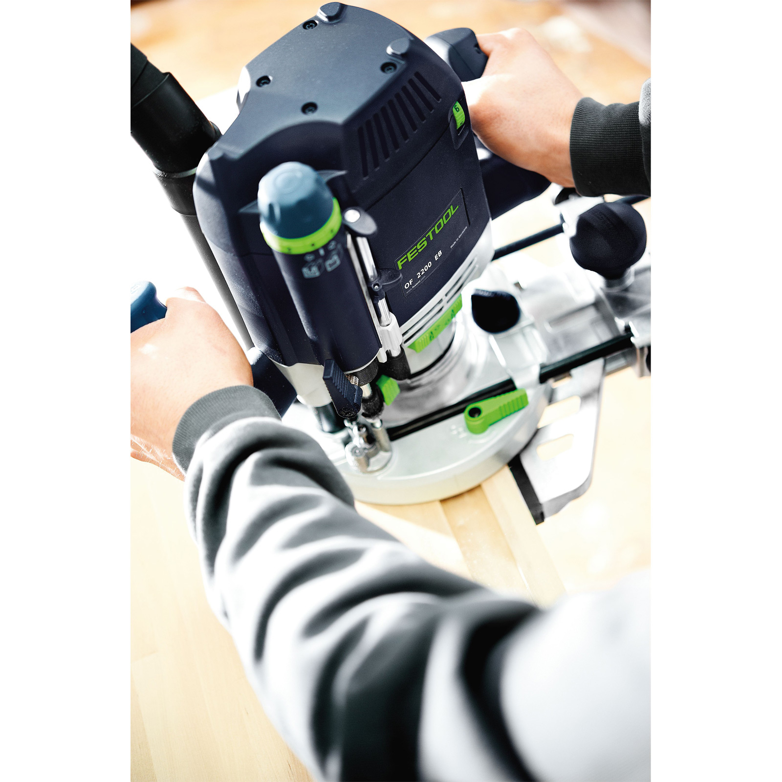 Una persona usa una fresatrice Festool OF 2200 EB. L'immagine mostra lo strumento in azione mentre taglia una tavola di legno.