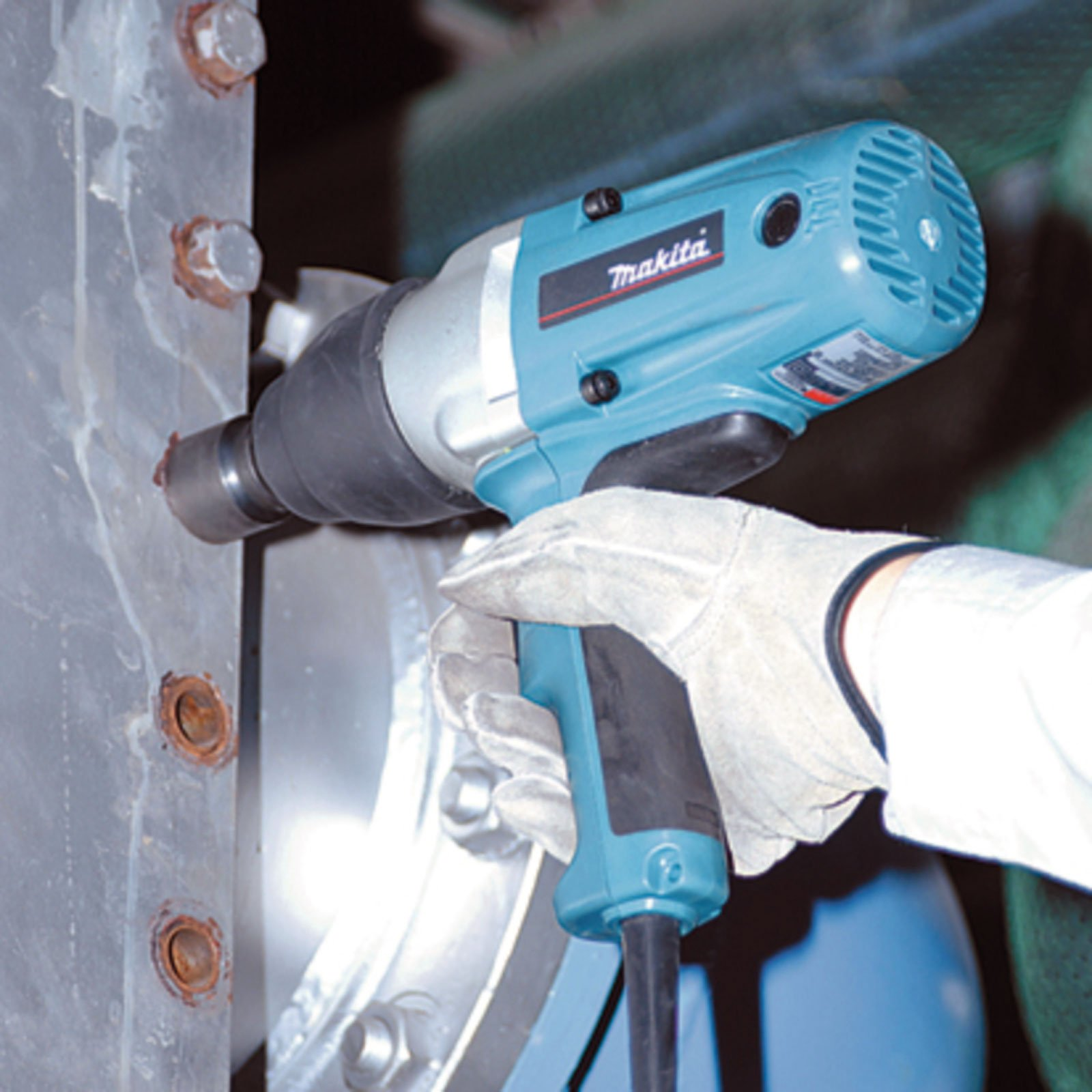 Eine Person benutzt einen Makita-Schlagschrauber auf einer Metalloberfläche mit Schrauben. Der Schraubenschlüssel ist blau und silber, gehalten von einer behandschuhten Hand.
