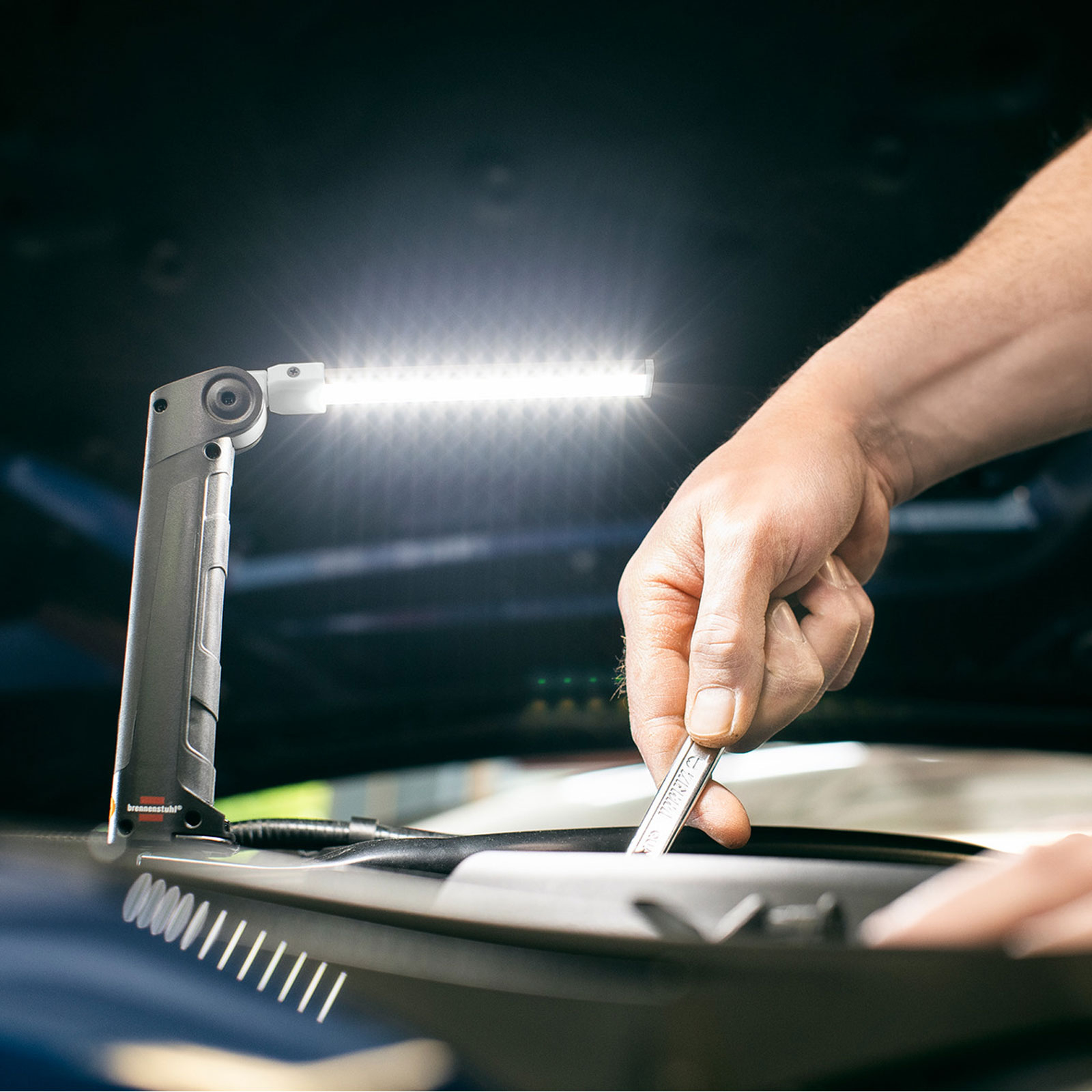 Mechanik używa klucza do pracy przy silniku samochodu, oświetlonego jasną lampą LED.