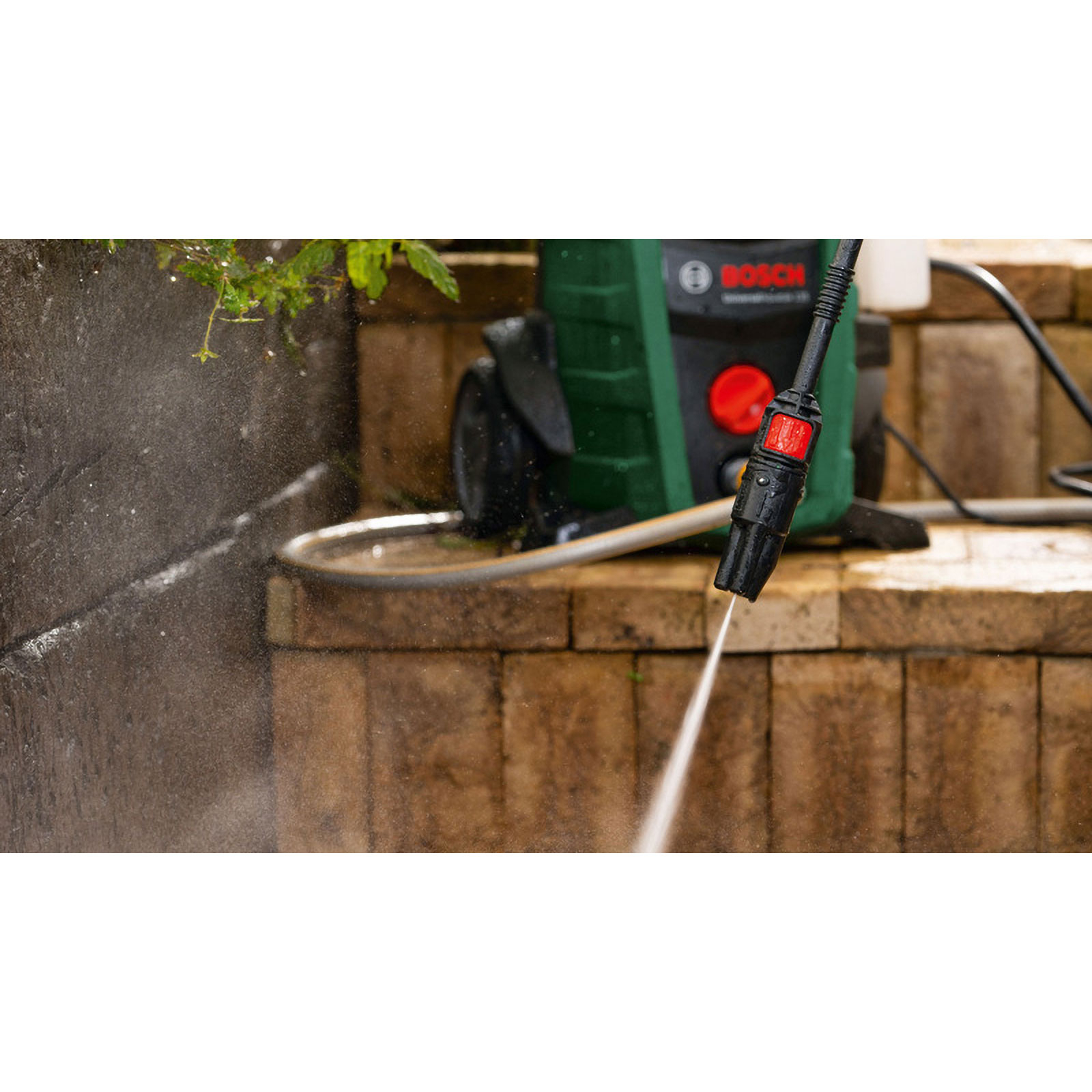 Ein Hochdruckreiniger sprüht Wasser. Grün-schwarze Maschine auf Ziegelsteinstufen. Wasserspray trifft eine Steinmauer und Stufen.