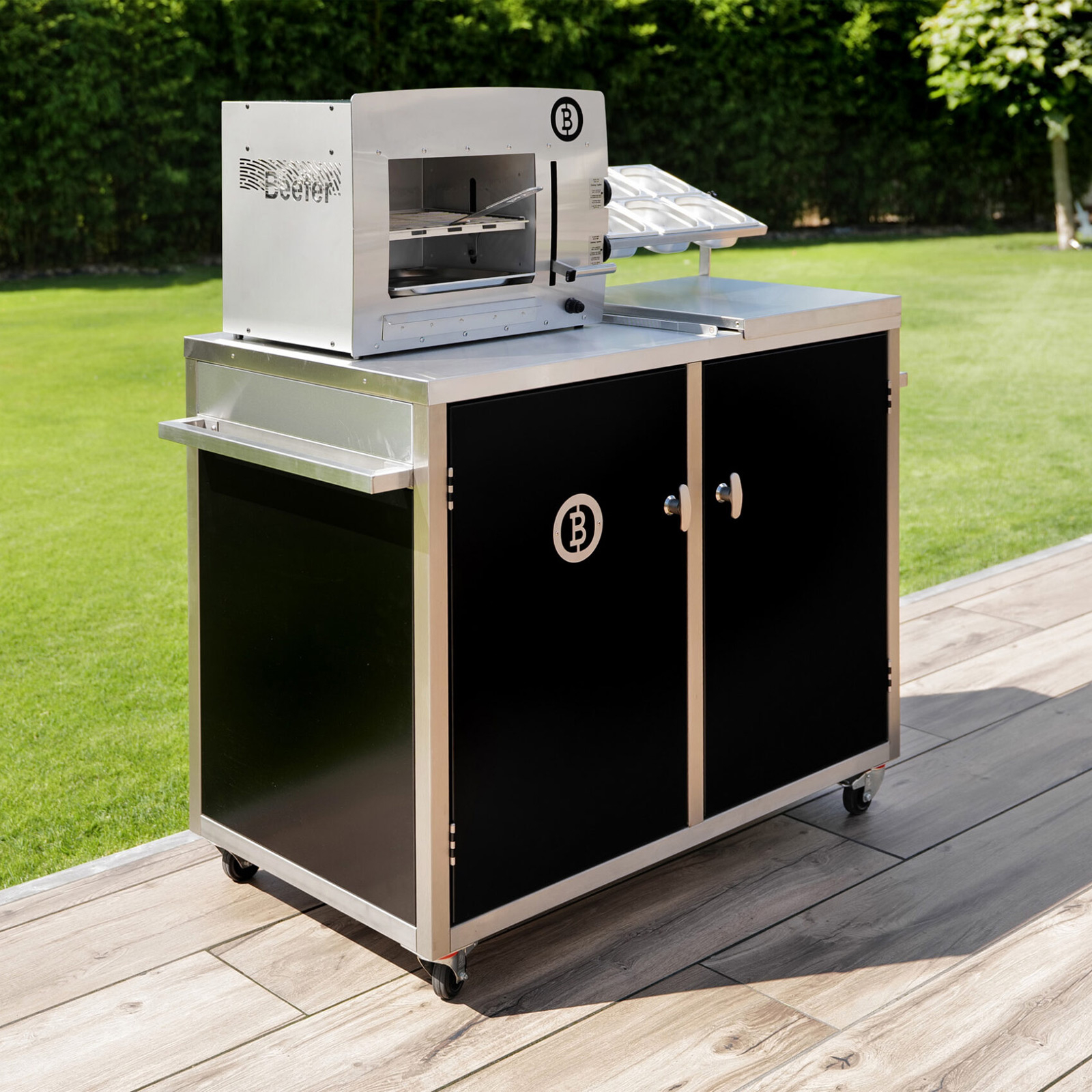 Ein Edelstahlgrill mit schwarzen Türen, einem 'B'-Logo und einer grünen Wiese im Hintergrund.