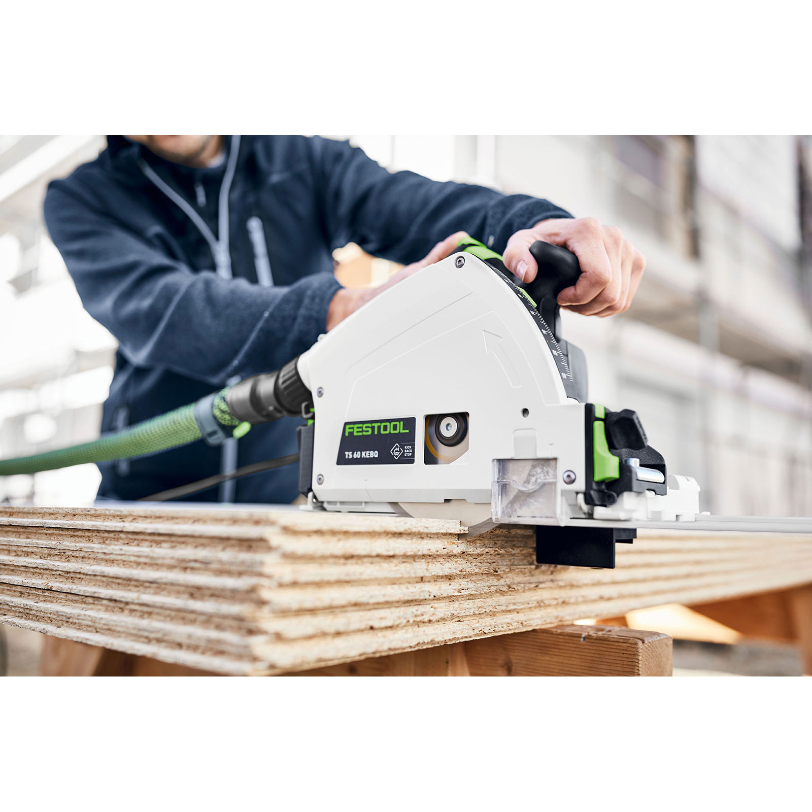 Eine Person schneidet mit einer Festool-Kreissäge Holz. Die Säge ist weiß und grün. Das Holz ist gestapelt. Der Hintergrund ist hell.