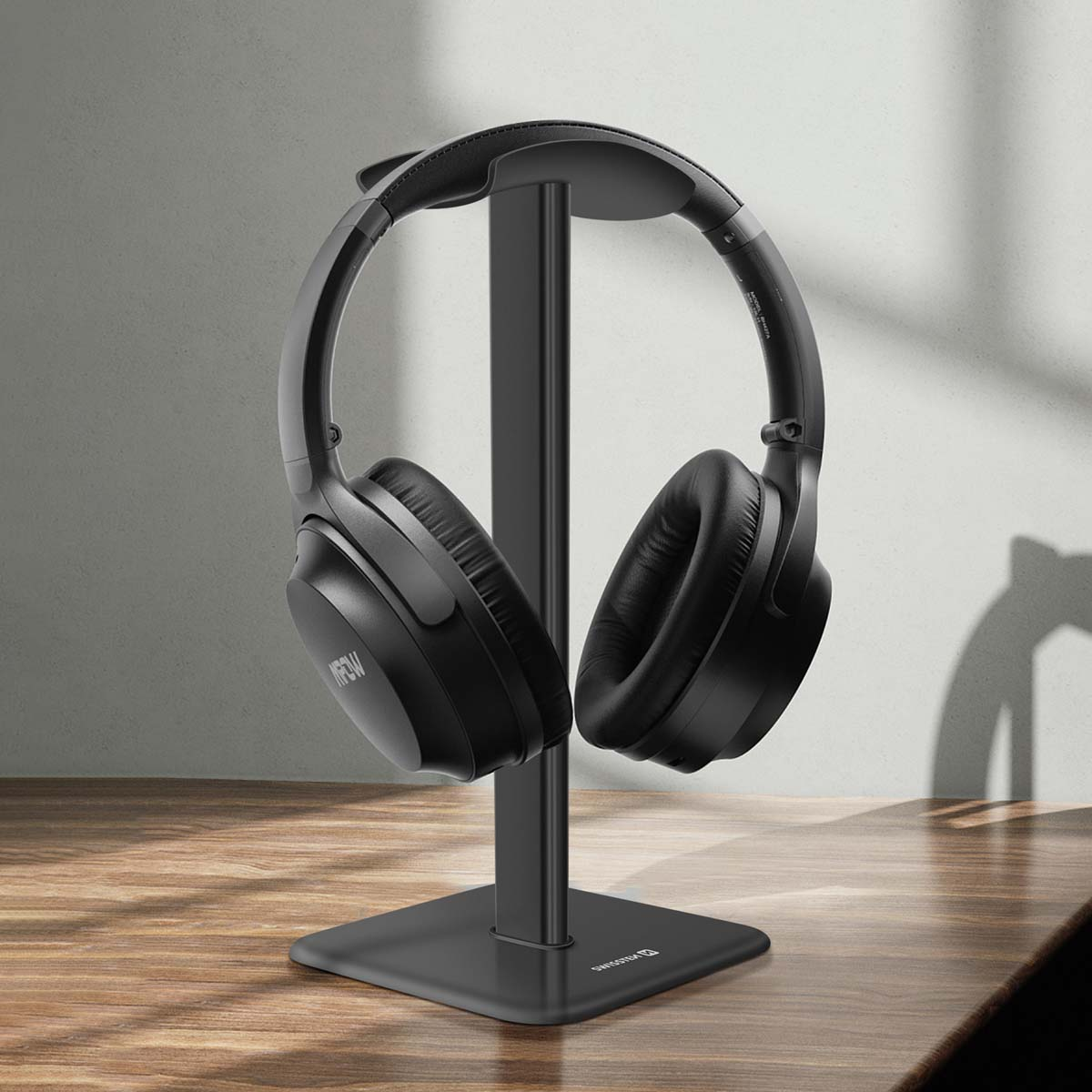 Auriculares negros sobre un soporte negro, colocados sobre una mesa de madera. El fondo es una pared gris claro con sombras.