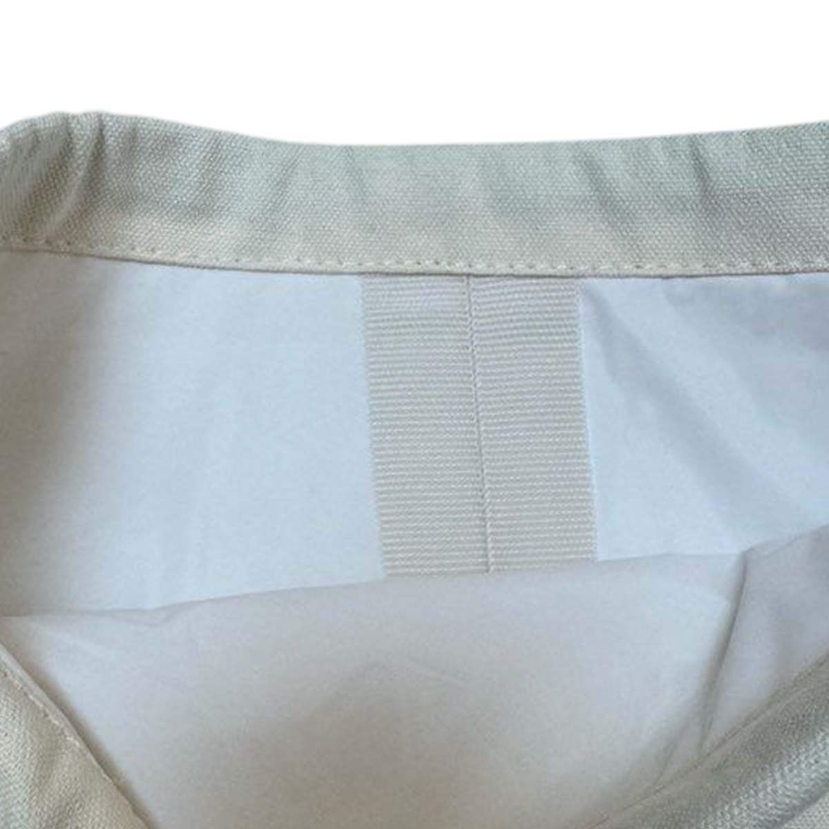 Nahaufnahme des Innenraums einer hellfarbigen Stofftasche. Sichtbar sind der obere Rand, das weiße Futter und ein vertikaler, beiger Riemen.