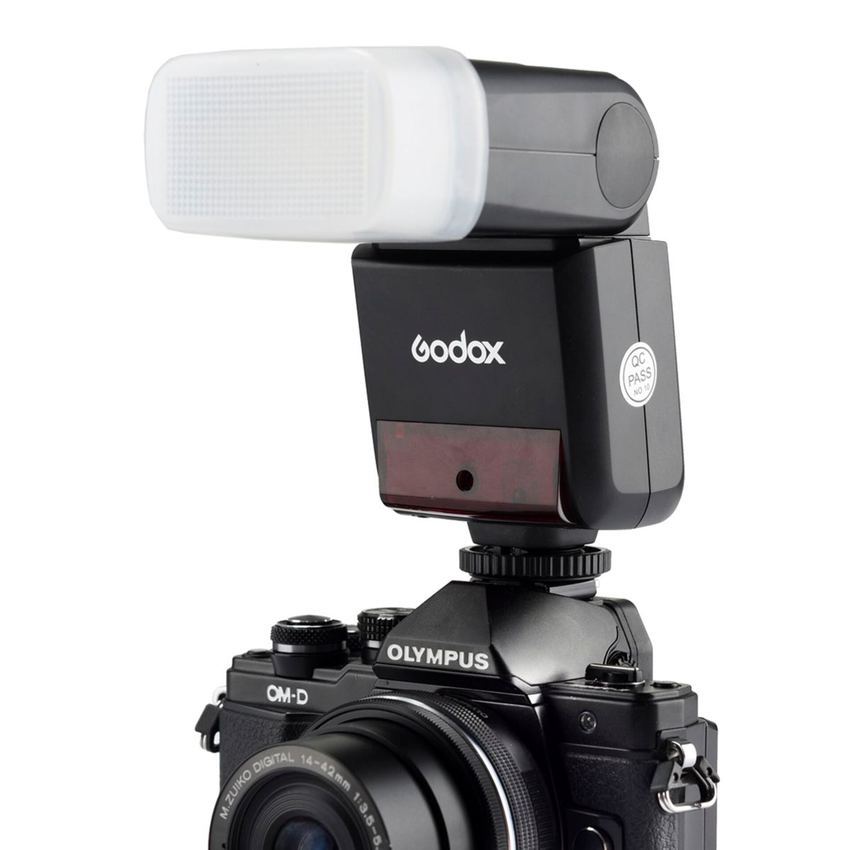 Un flash Godox noir est monté sur un appareil photo Olympus. Le flash a un diffuseur blanc. L'appareil photo a un objectif.