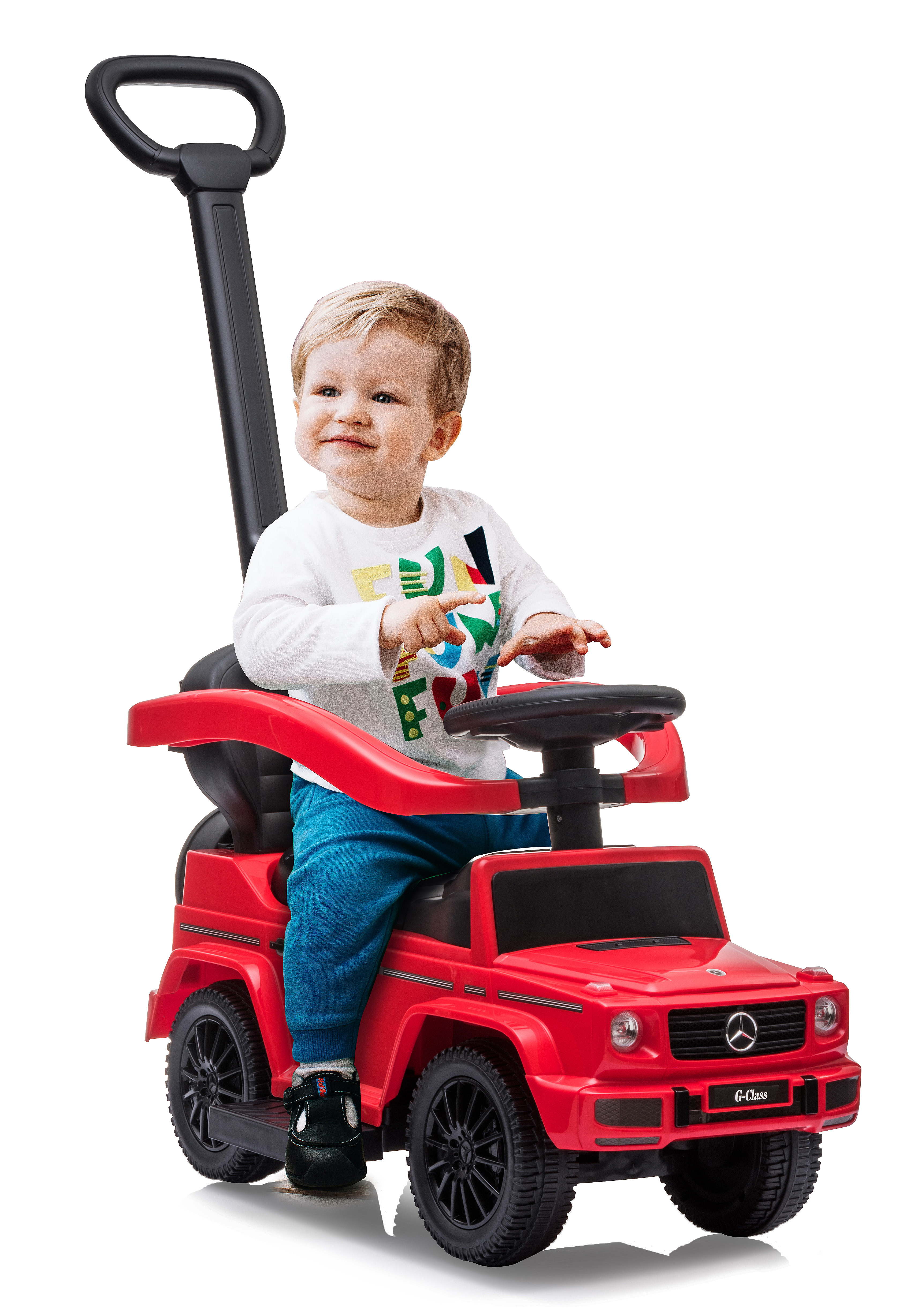 Ein Kleinkind sitzt in einem roten Spielzeugauto. Er trägt ein weißes Hemd und eine blaue Hose. Das Auto hat einen schwarzen Griff.