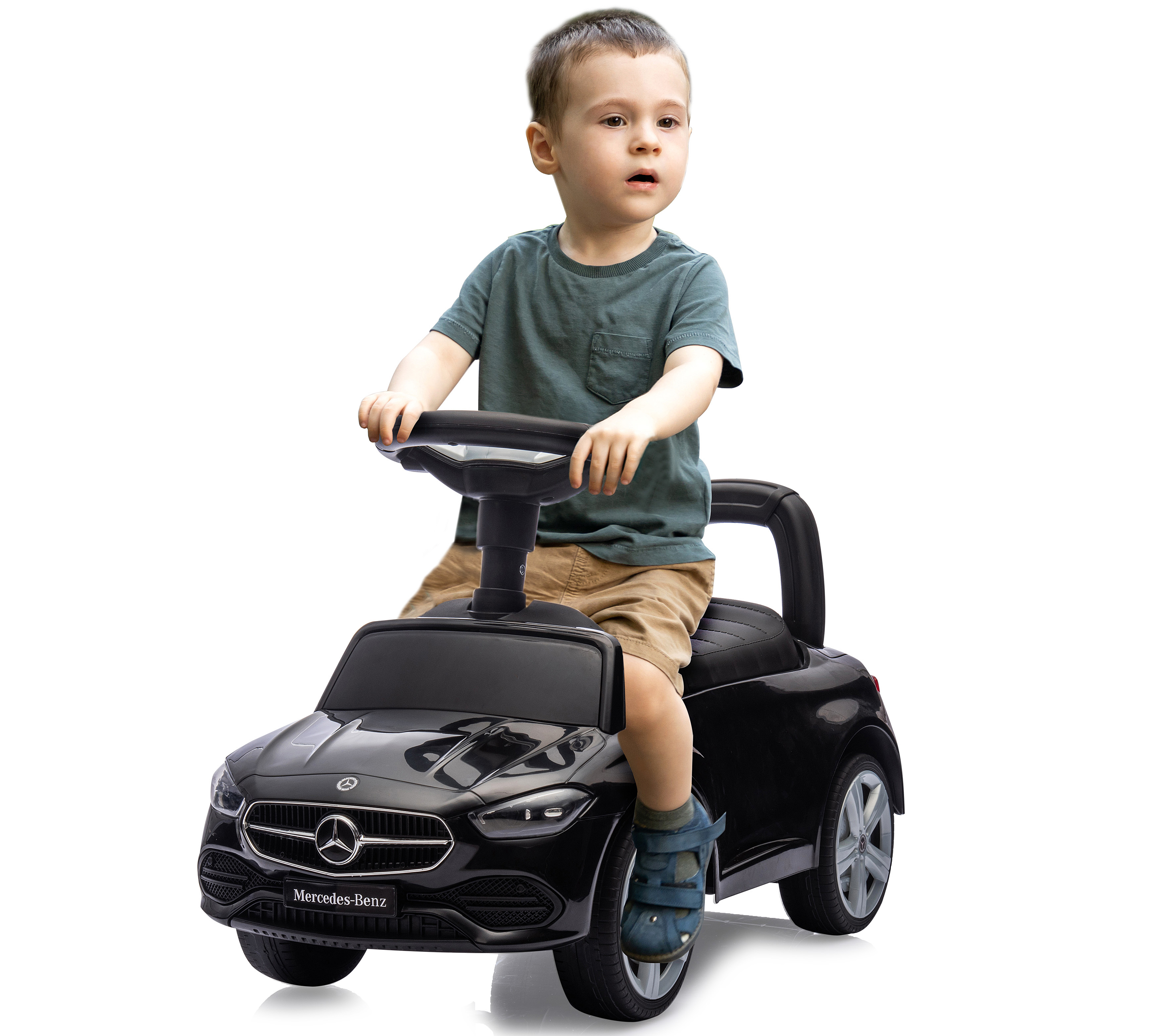 Ein kleiner Junge sitzt in einem schwarzen Mercedes-Benz Spielzeugauto. Er trägt ein türkisfarbenes Hemd und Shorts. Das Auto steht vor weißem Hintergrund.