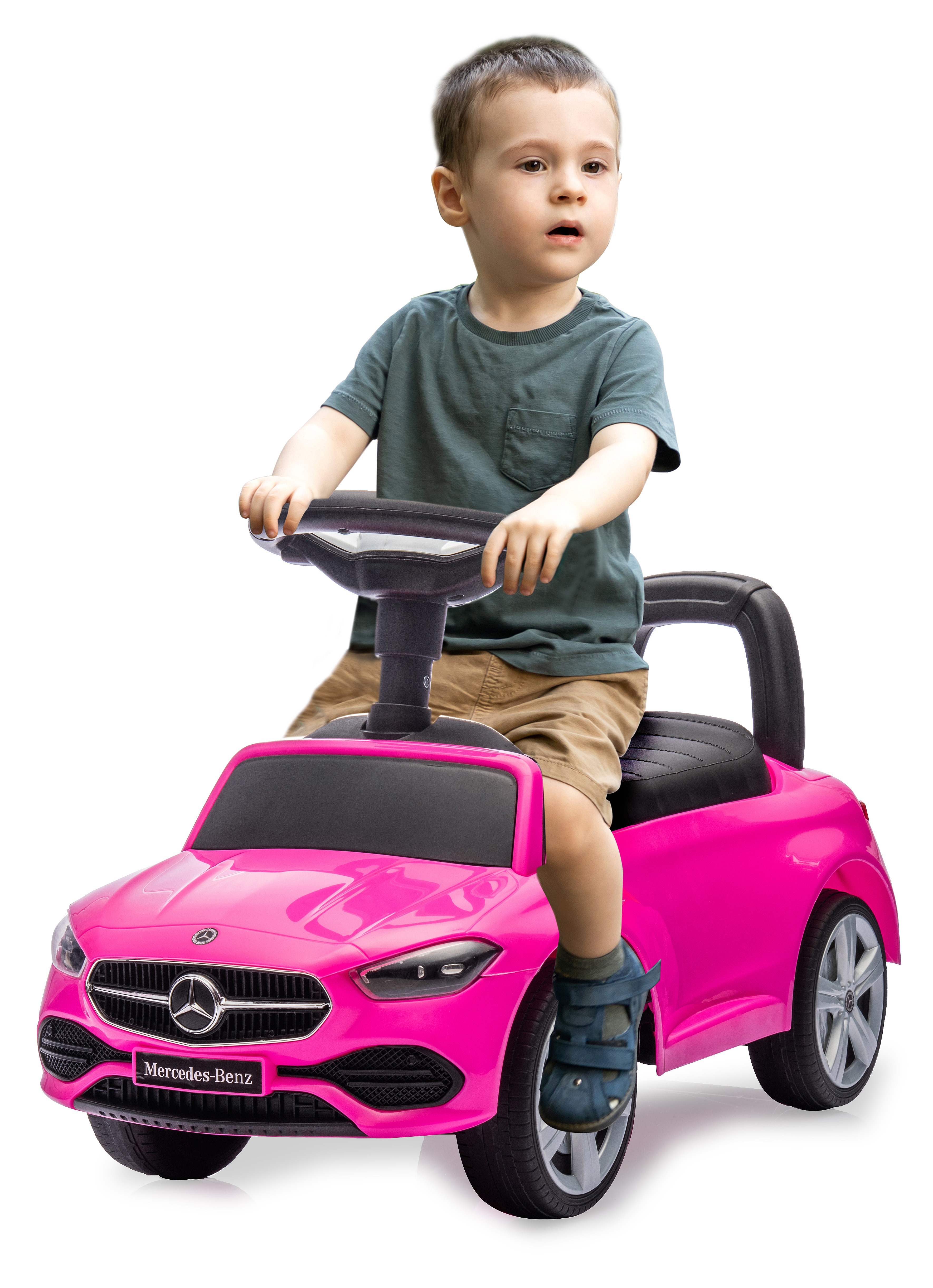 Ein kleiner Junge sitzt in einem rosa Mercedes-Benz Spielzeugauto. Er trägt ein grünes Hemd und khakifarbene Shorts. Das Auto hat schwarze Räder.