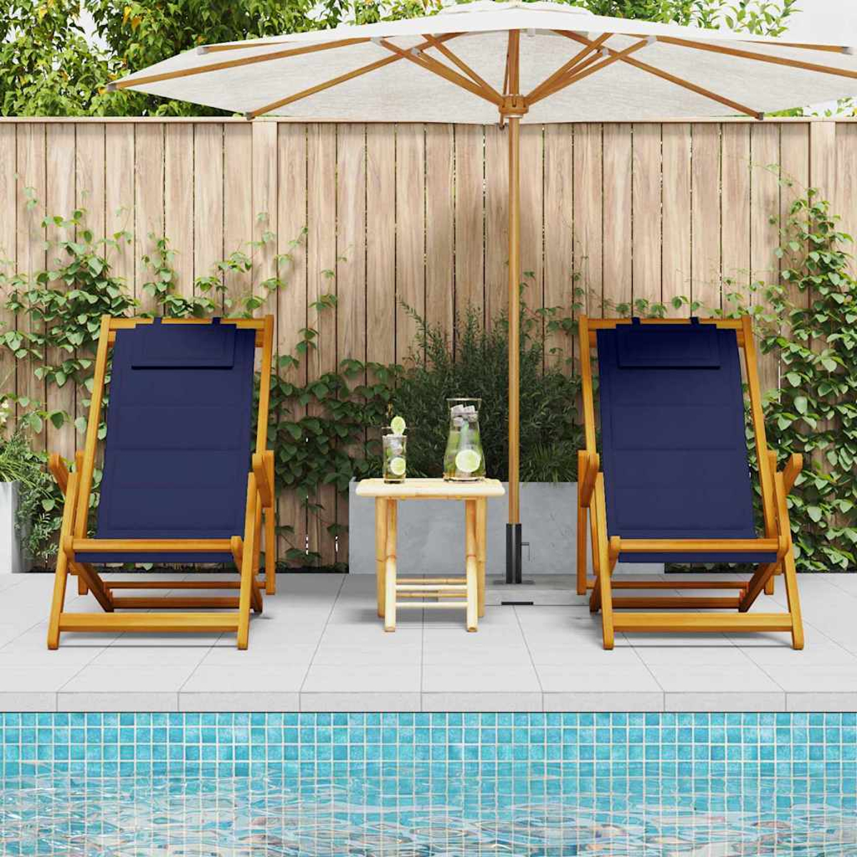 Zwei blaue Liegestühle stehen sich an einem Pool gegenüber. Ein kleiner Tisch mit Getränken steht dazwischen. Ein Schirm spendet Schatten.
