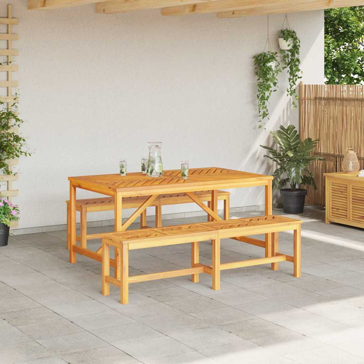 Juego de comedor de madera al aire libre con mesa y bancos. Bebidas en la mesa, plantas y una valla de bambú al fondo.