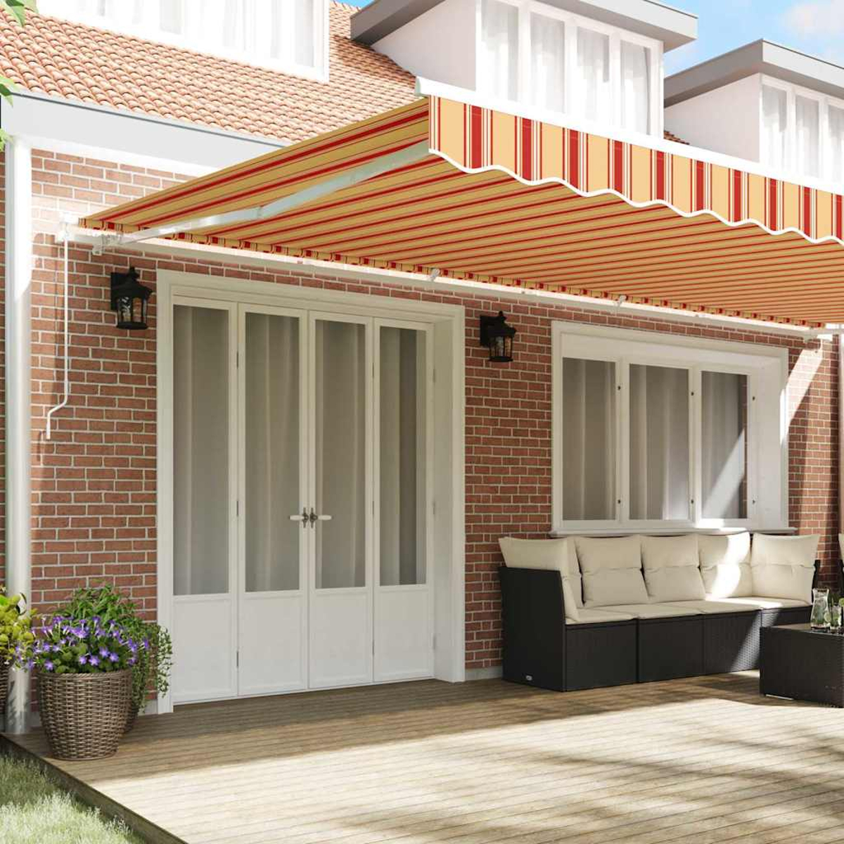 Ein Haus mit roter Backsteinfassade, einer ausziehbaren gestreiften Markise, weißen Türen und einer Terrasse mit Möbeln.
