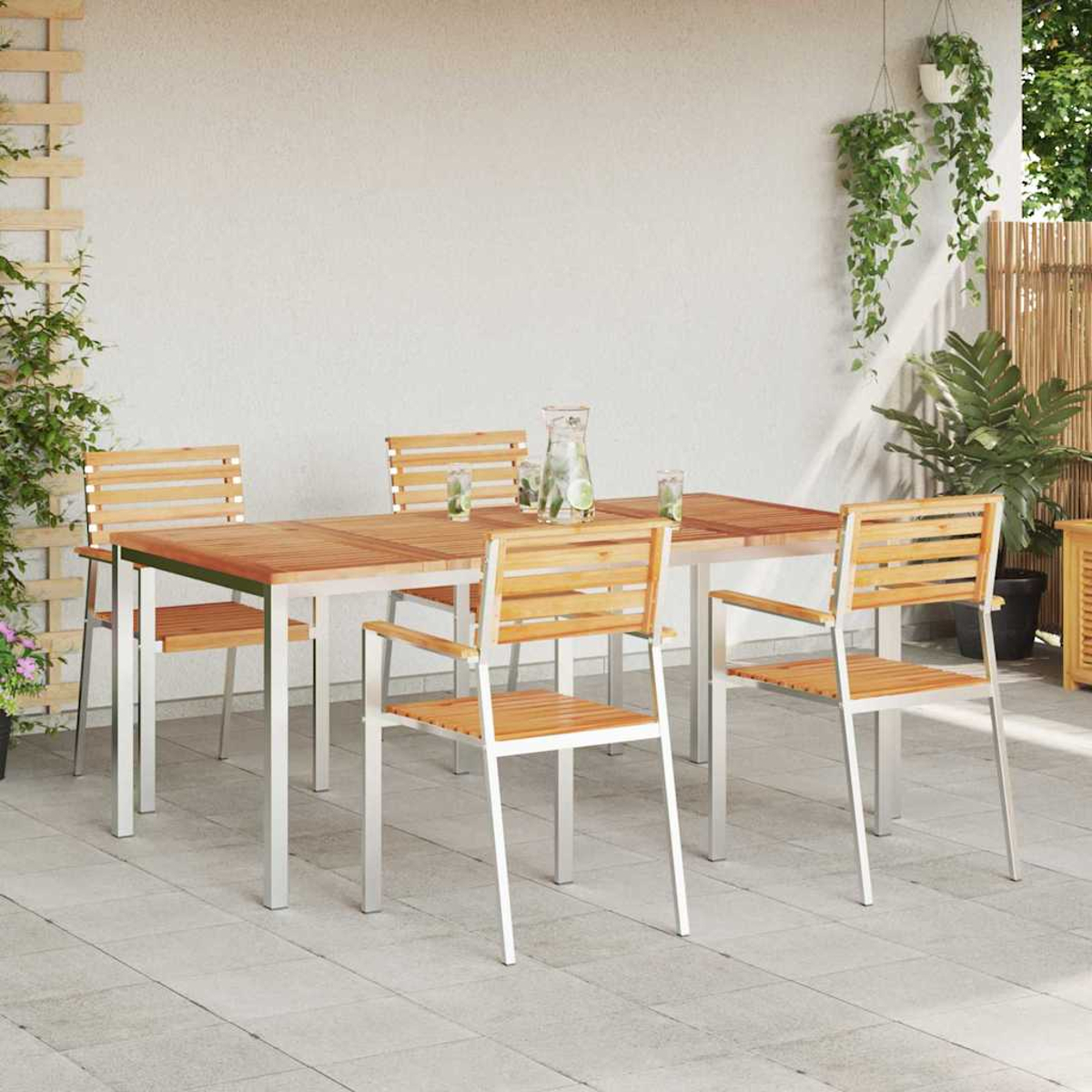 Essgruppe im Freien: Holztisch und Stühle auf einer Terrasse. Pflanzen schmücken den Hintergrund, Krug und Gläser auf dem Tisch.