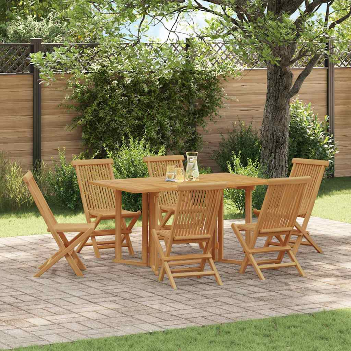 Holztisch und Stühle auf einer Terrasse. Ein Baum spendet Schatten. Hintergrund ist ein Holzzaun und Grün.