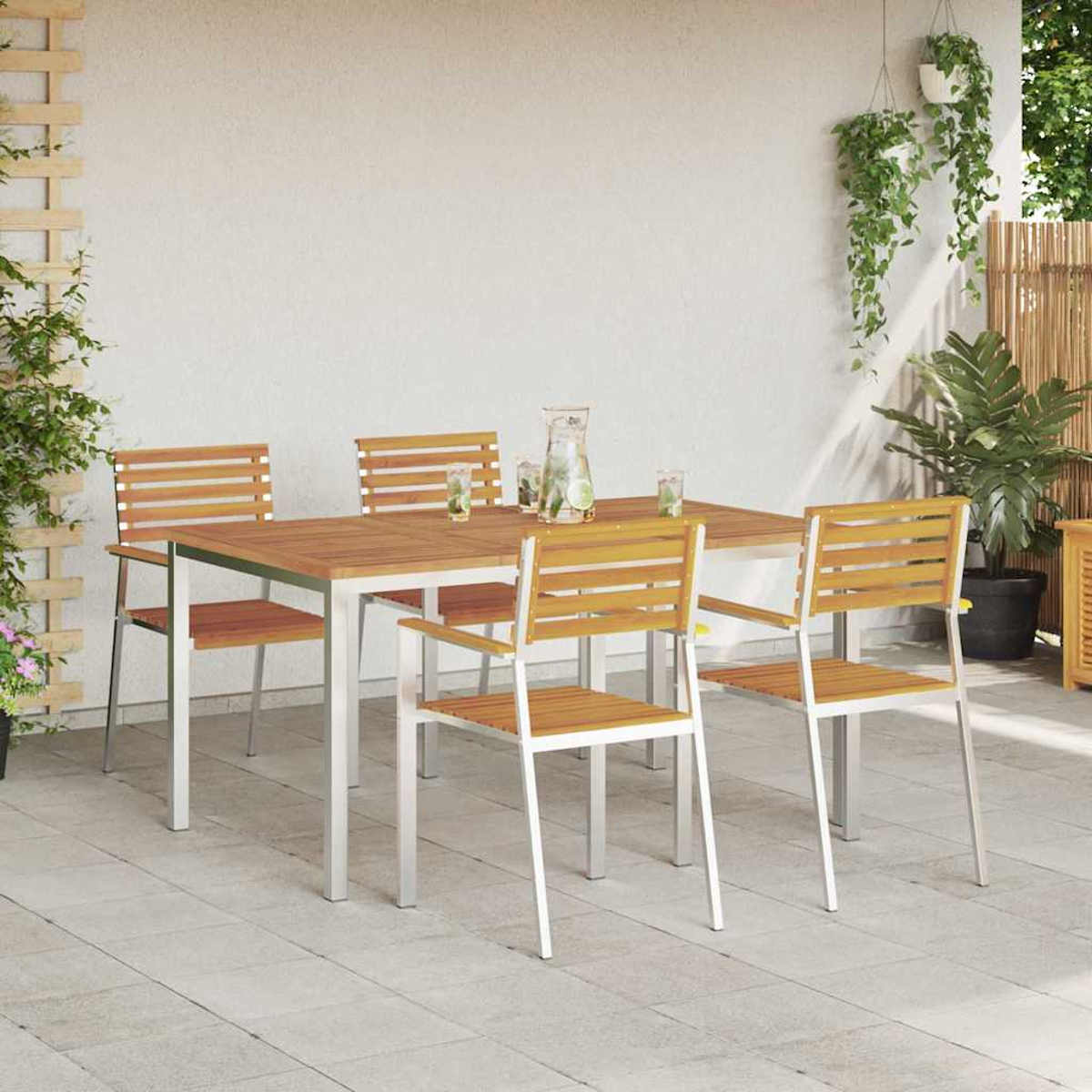 Essgruppe im Freien auf einer Terrasse. Ein Holztisch mit vier Stühlen, eine Wasserkaraffe und Gläser. Pflanzen und eine weiße Wand im Hintergrund.