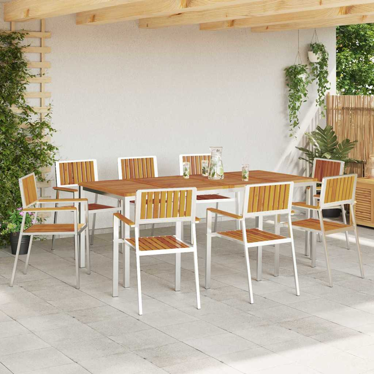 Essgruppe im Freien. Holztisch, umgeben von Stühlen mit Metallrahmen. Auf dem Tisch stehen ein Krug und Gläser. Pflanzen dekorieren den Hintergrund.