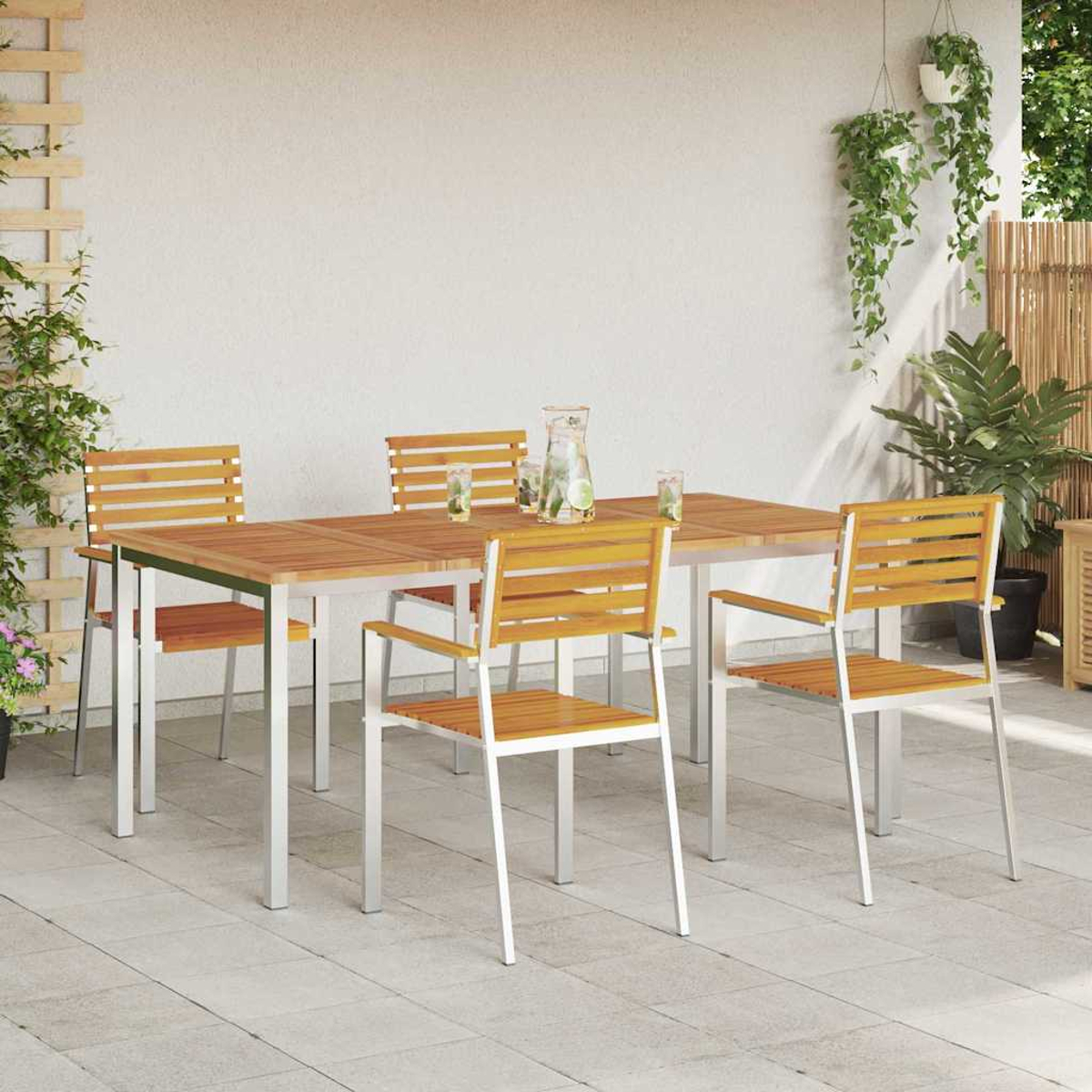 Essgruppe im Freien: Holztisch und Stühle, Wasserkrug mit Gläsern, auf einer gefliesten Terrasse, mit Pflanzen im Hintergrund.