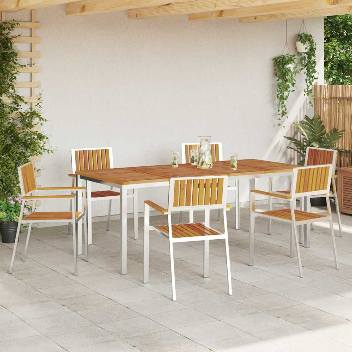 Essgruppe im Freien mit Holztisch und Stühlen. Pflanzen hängen von der Decke und wachsen an der Seitenwand. Gläser und eine Kanne auf dem Tisch.