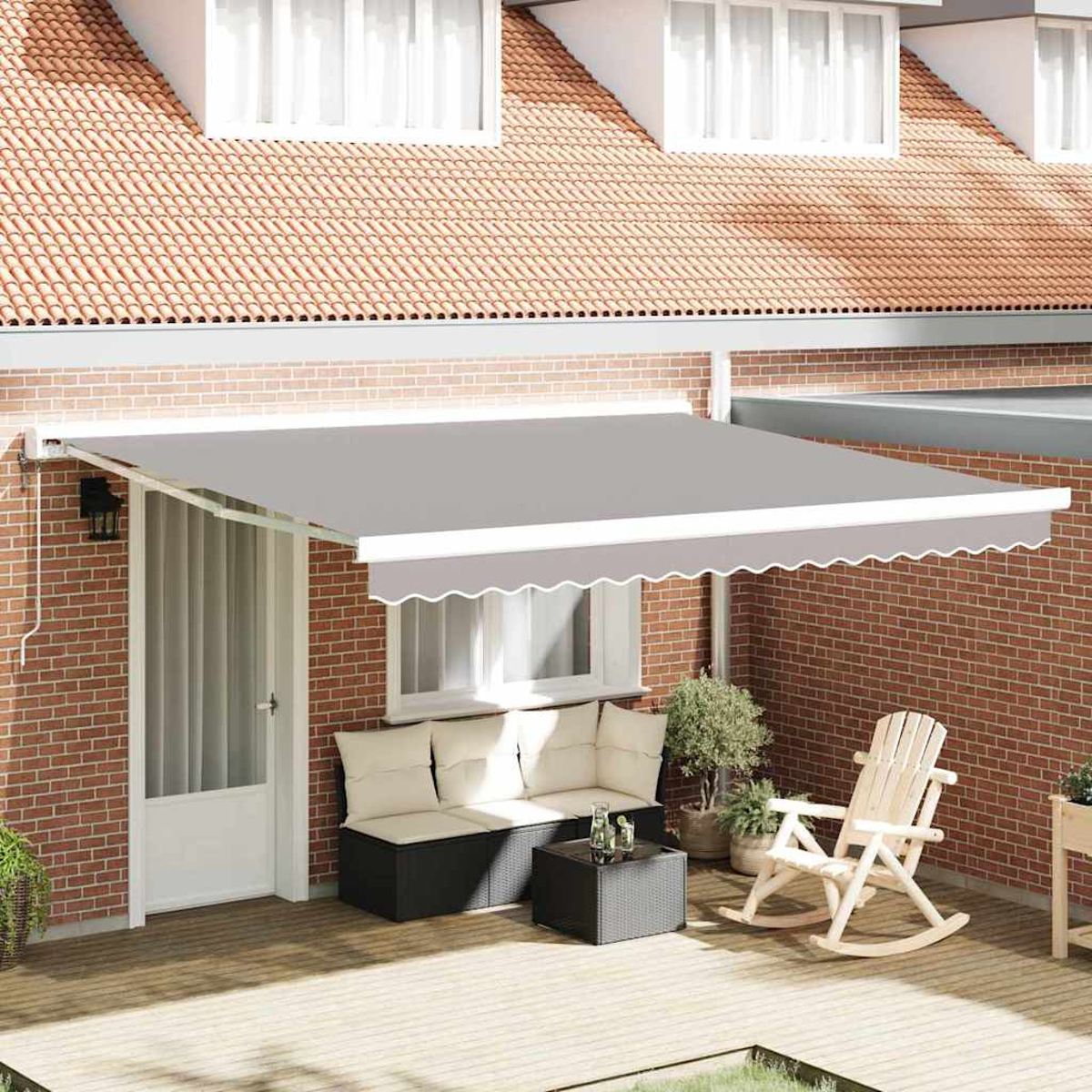 Eine Terrasse mit grauem Sonnensegel, Backsteinmauer, weißer Tür, Sitzgelegenheiten, Schaukelstuhl und rotem Ziegeldach im Hintergrund.