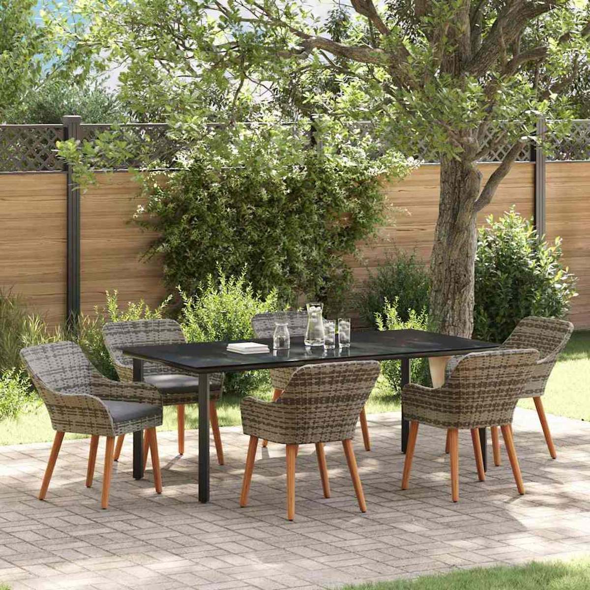 Un juego de comedor al aire libre con mesa negra, seis sillas, vaso de agua en patio de ladrillo, rodeado de árboles y valla de madera.