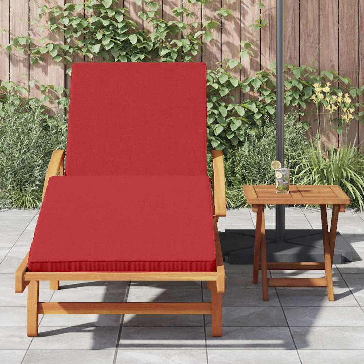 Ein roter Liegestuhl mit Kissen neben einem kleinen Holztisch mit einem Getränk. Der Hintergrund ist ein Holzzaun und Grün.