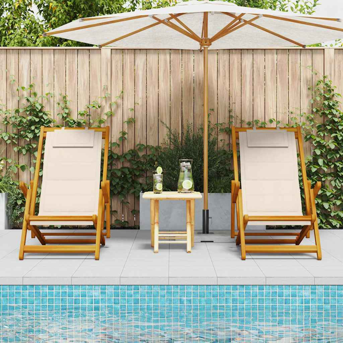 Zwei beige Liegestühle, ein kleiner Tisch mit Getränken und ein weißer Sonnenschirm in der Nähe eines Pools. Holzzaun und Laub im Hintergrund.