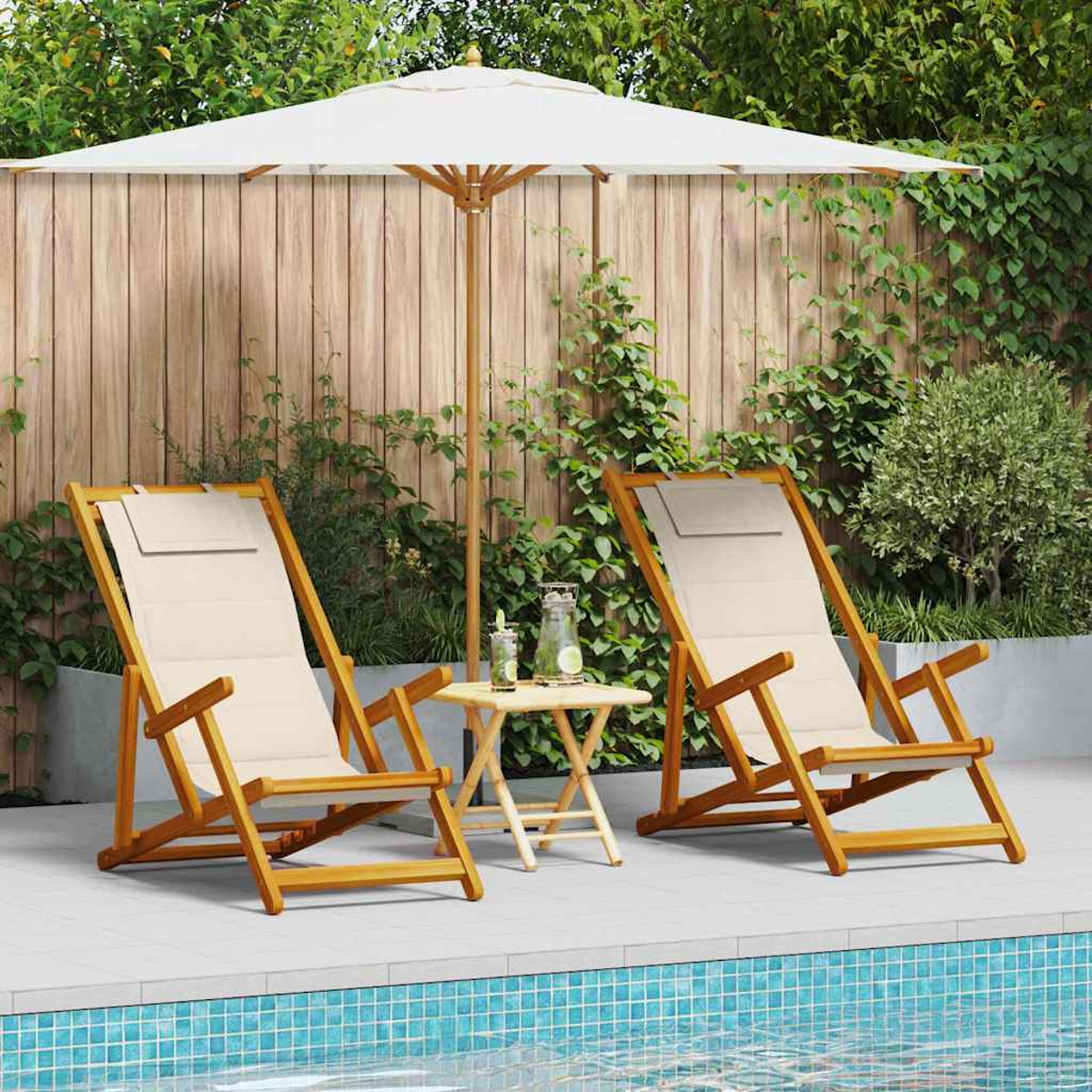 Zwei Holzliegen mit cremefarbenem Stoff, ein kleiner Tisch und ein weißer Sonnenschirm am Pool. Im Hintergrund ein Holzzaun.