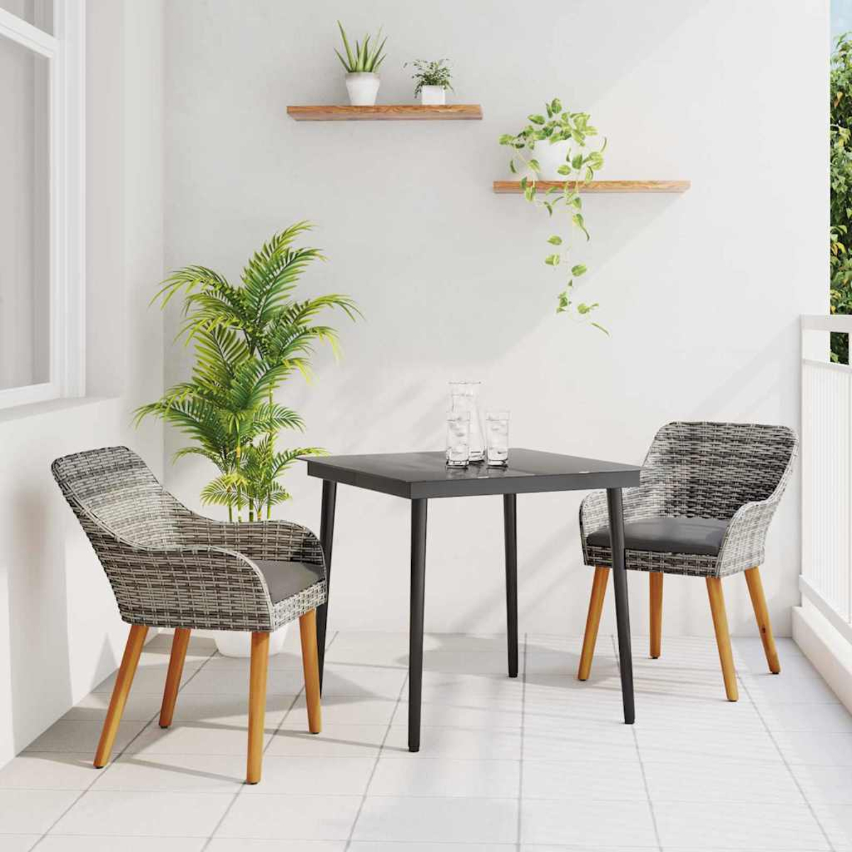 Balkonszene mit schwarzem Tisch, zwei Stühlen und Pflanzen. Zwei Gläser auf dem Tisch. Weiße Wände, Fliesenboden und Holzregale.